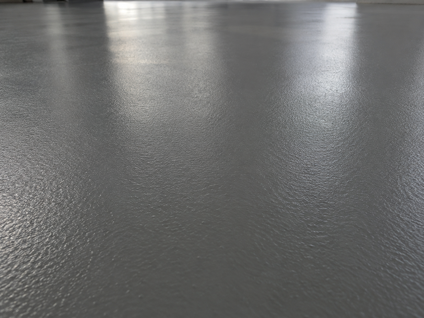 Close-up of a smooth, shiny, gray polished concrete floor with reflections.