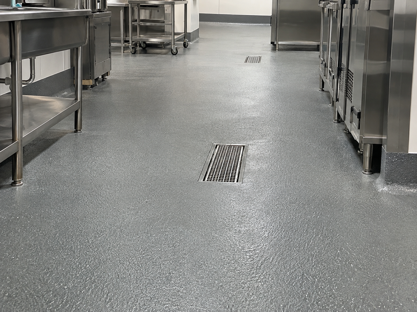 Industrial kitchen with stainless steel equipment and a textured, non-slip gray floor with floor drains.
