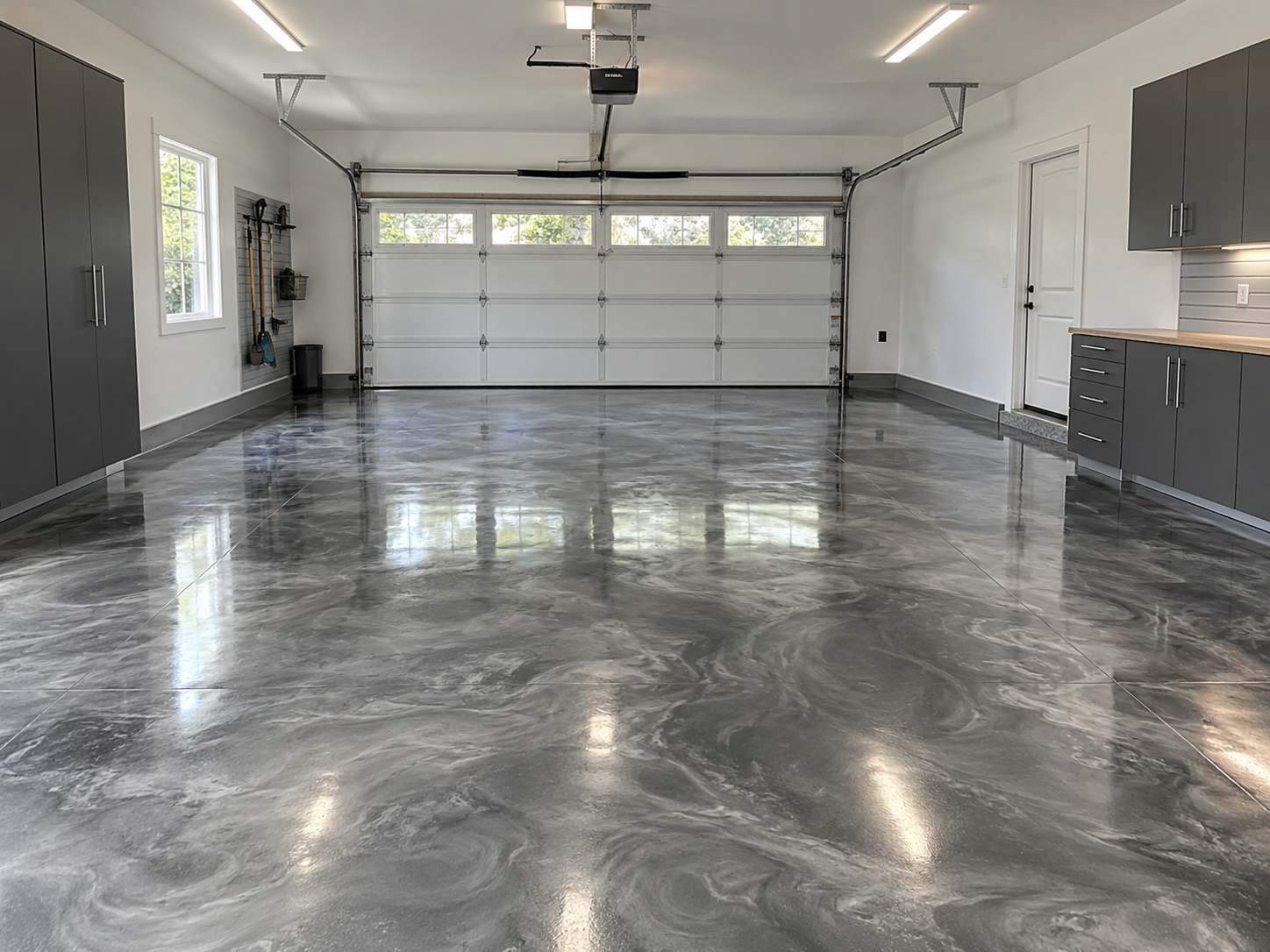 Spacious, clean garage with polished concrete floors, gray cabinets, a large white garage door with windows, and a window on the left wall.