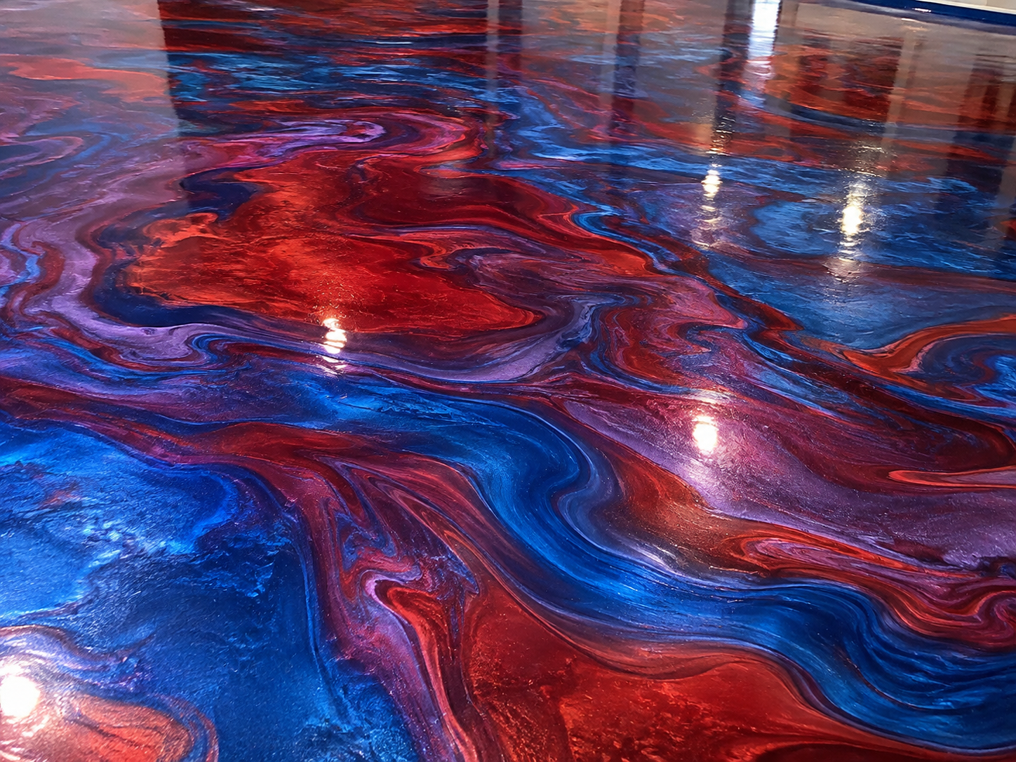 Close-up of a colorful abstract painting with swirling patterns in shades of red, blue, purple, and hints of white, reflecting light.