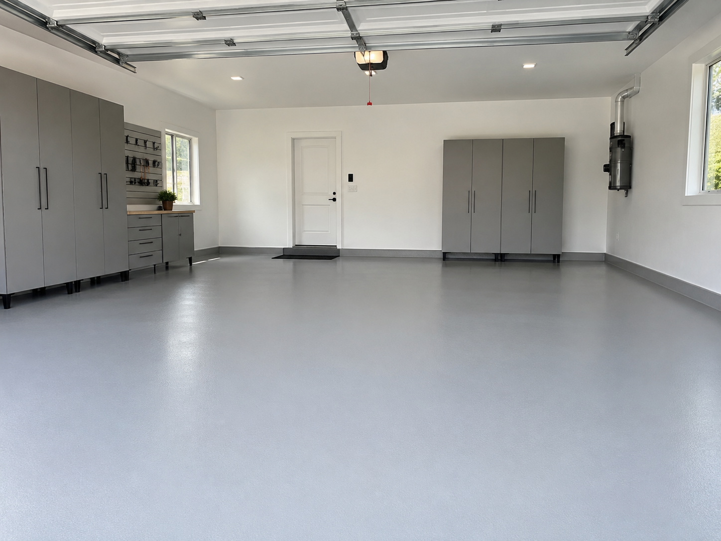 Empty garage with gray cabinets, a workbench, a window, and a garage door opener.