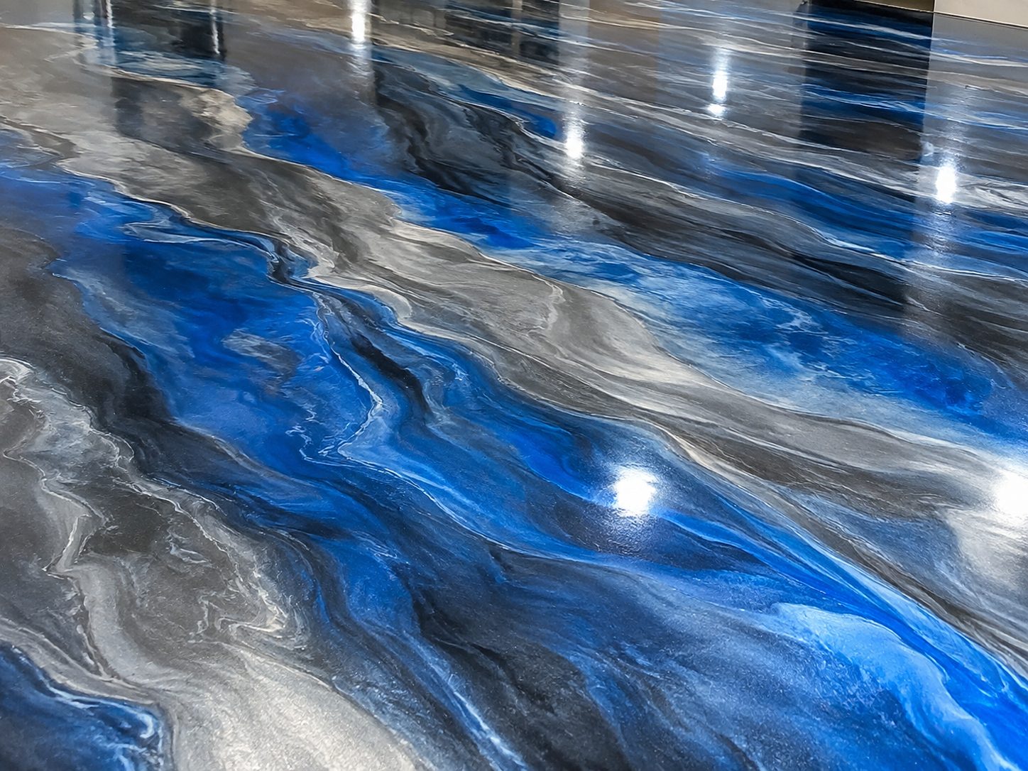 Close-up of an abstract floor with swirling patterns in shades of black, gray, blue, and white, resembling river currents or marble veins.