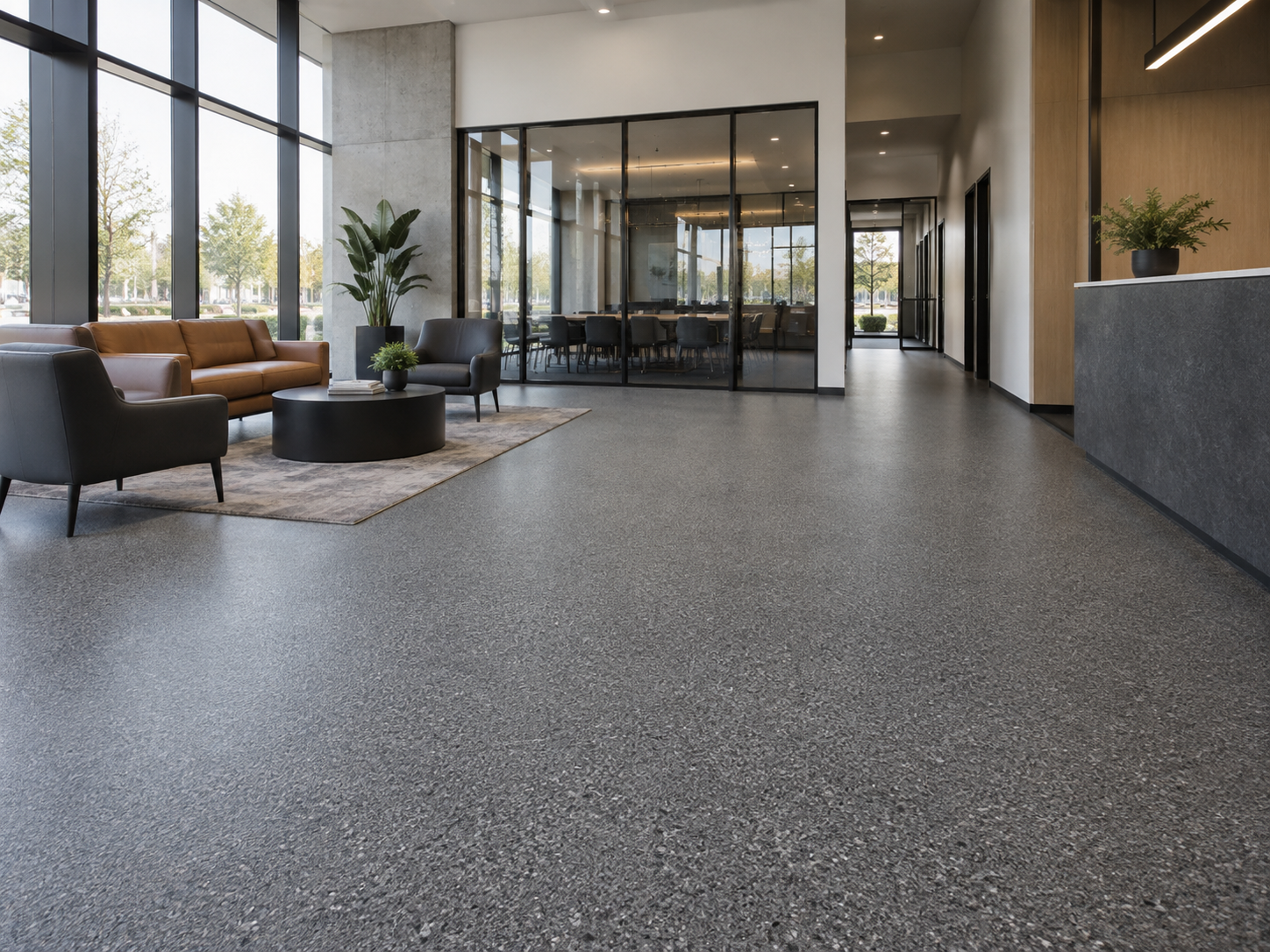 Modern lobby area with leather and fabric chairs, a round black coffee table, large glass windows, a rug, potted plants, and a conference room with glass walls in the background.