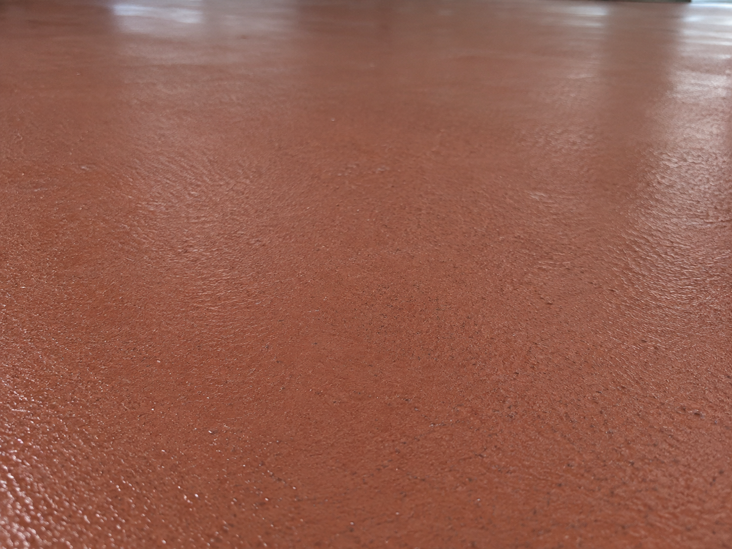 Close-up of a textured, reddish-brown surface, possibly a painted or coated floor.
