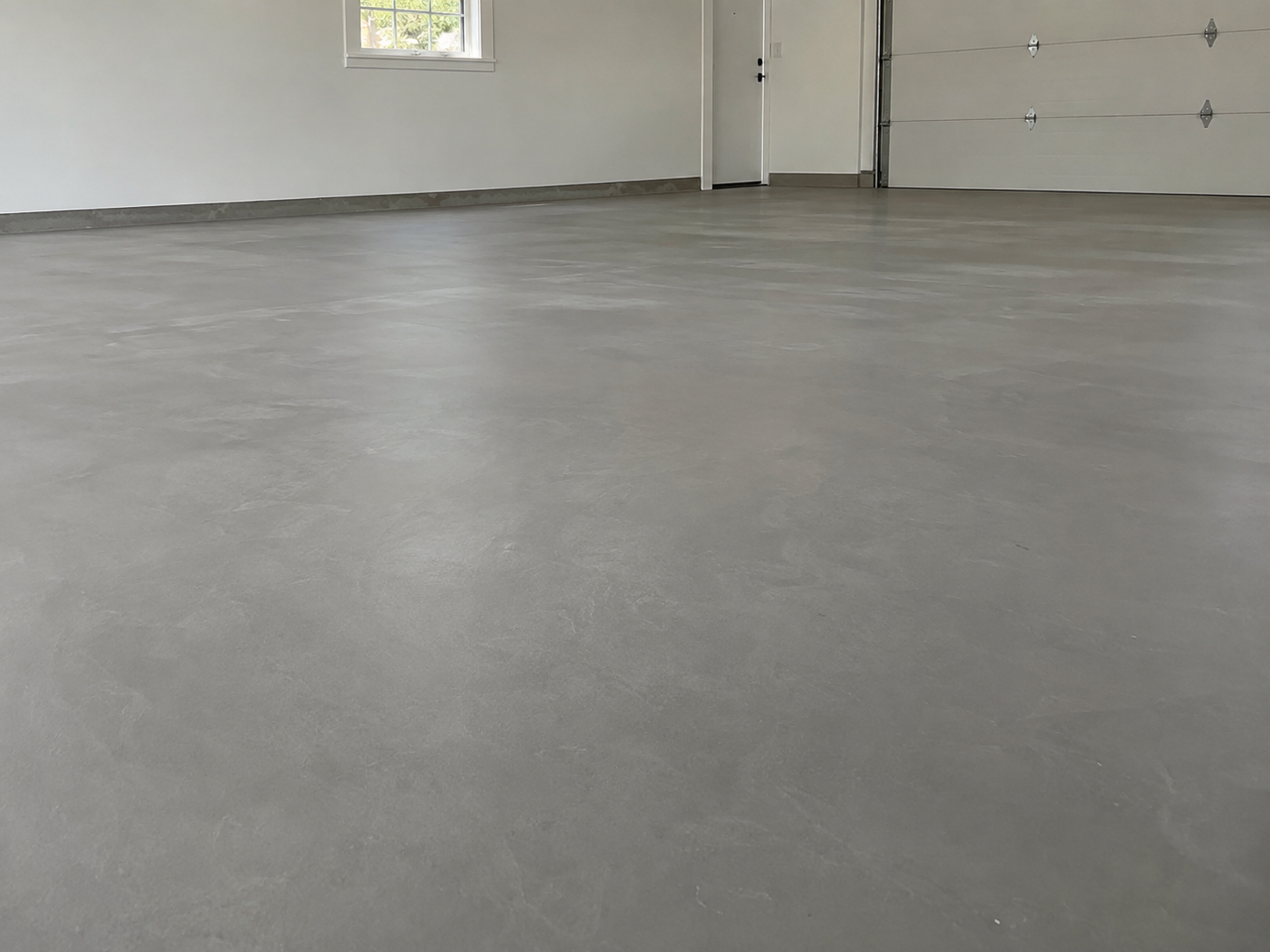 Empty garage with polished concrete floor, white walls, a window, and a closed garage door.