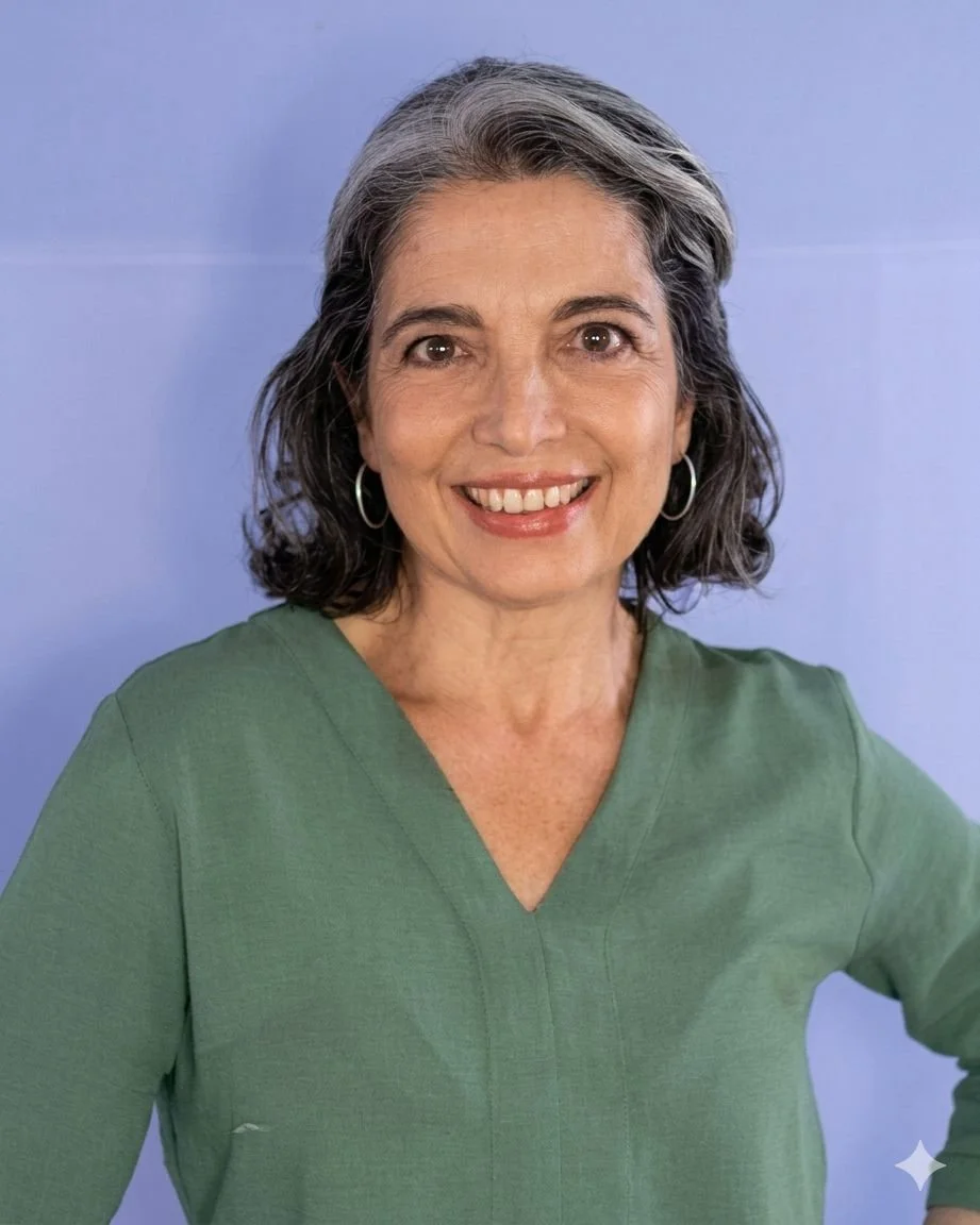 Retrato de una mujer de cabello corto gris, con aretes de aro, sonriendo y usando blusa verde, contra un fondo azul.