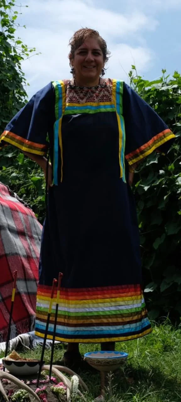 Mujer con vestido tradicional mexicano de colores en un campo con vegetación, durante el día.