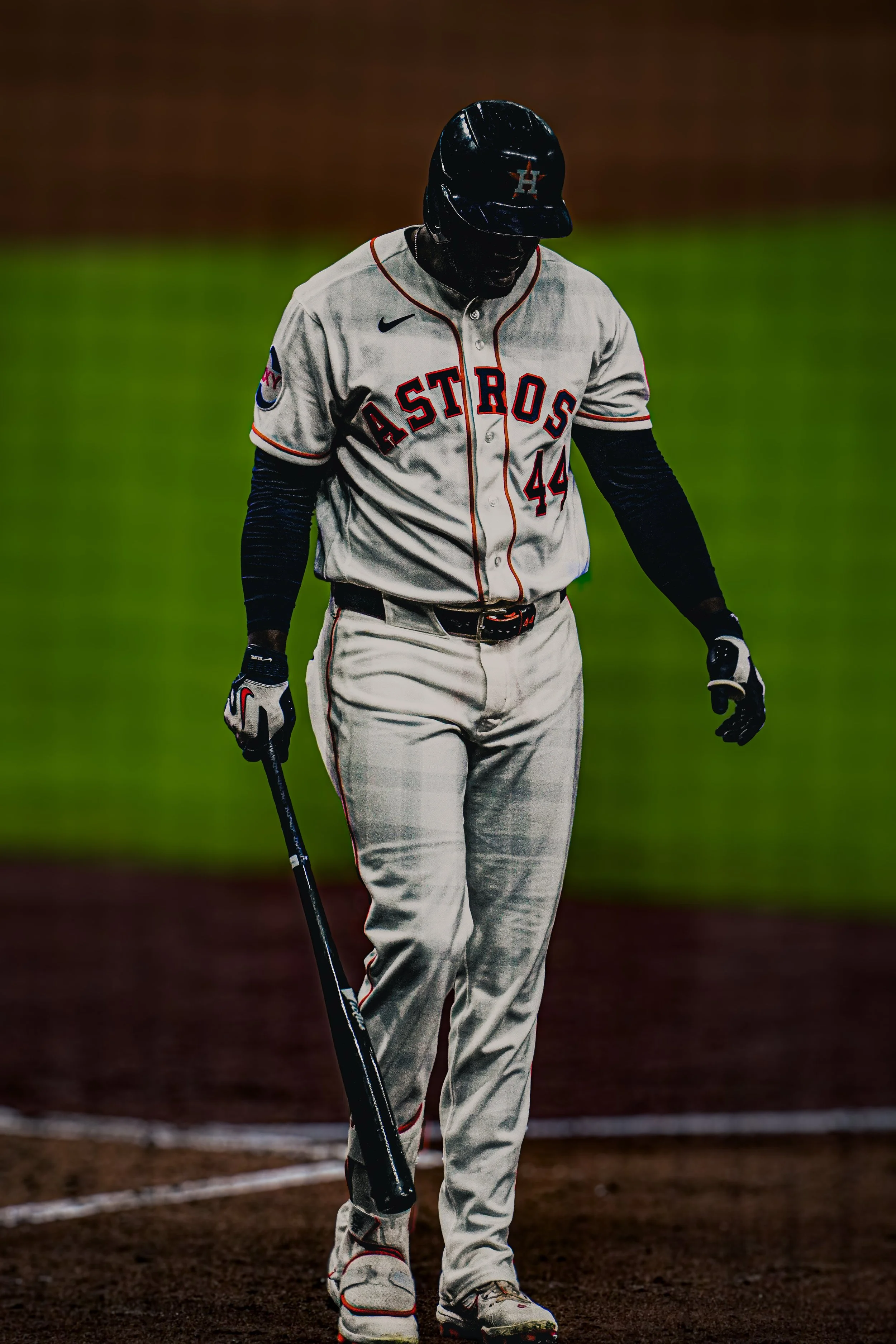 A baseball player wearing a Houston Astros jersey and cap, standing on the field with his head bowed.