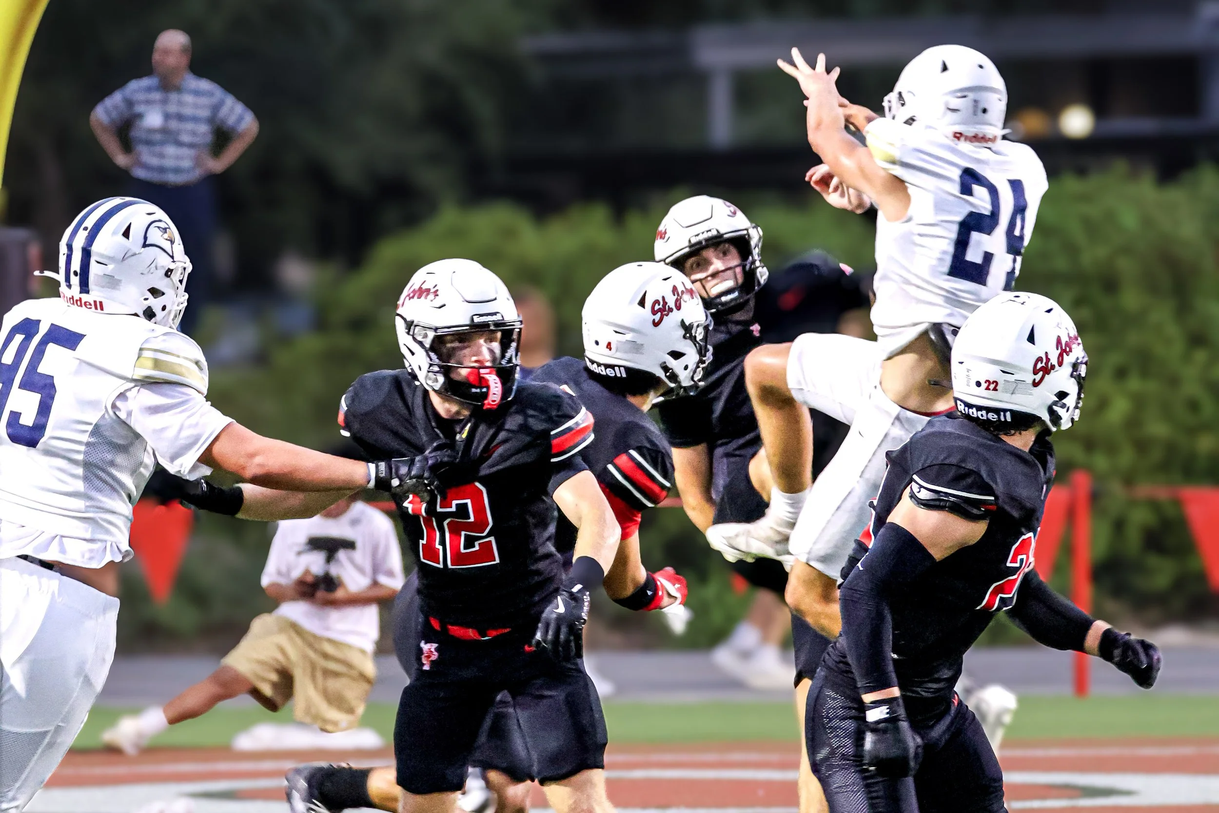 A group of football players in white and black uniforms competing during a game, with one player jumping to catch the ball.