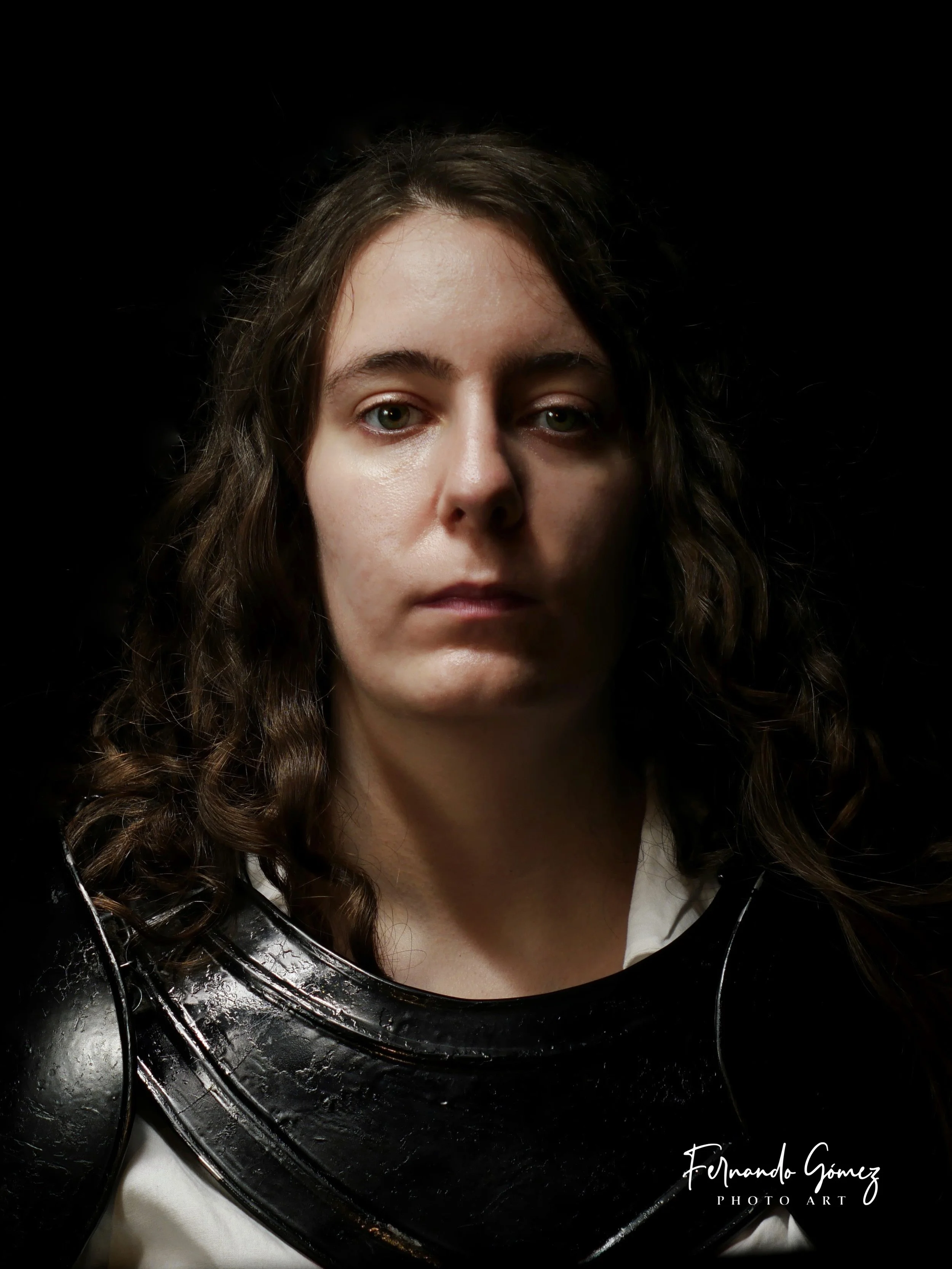 A woman with wavy brown hair and green eyes facing the camera, wearing a white shirt and black leather jacket, against a black background.