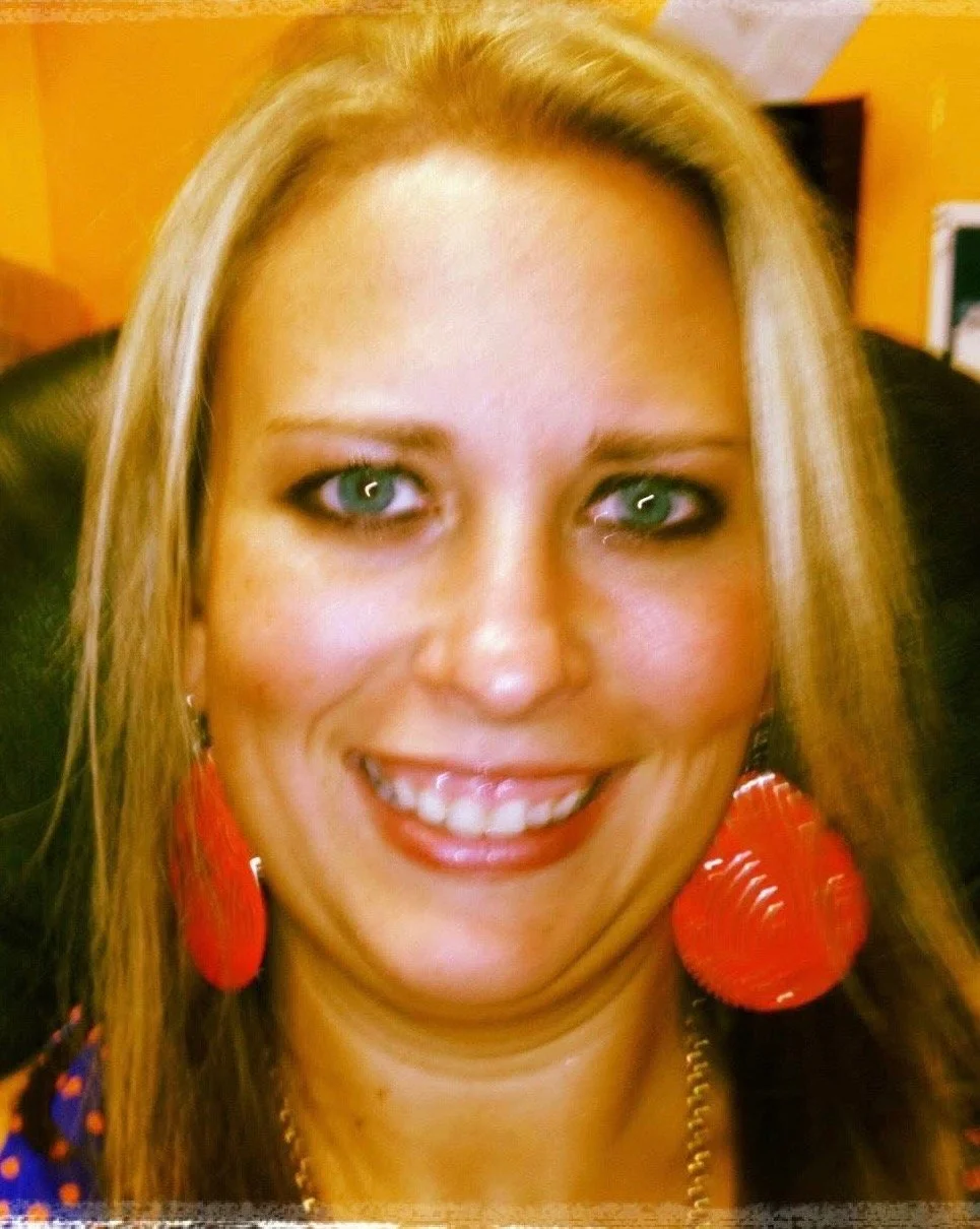 A woman with blonde hair, blue eyes, and wearing large red earrings, smiling at the camera.