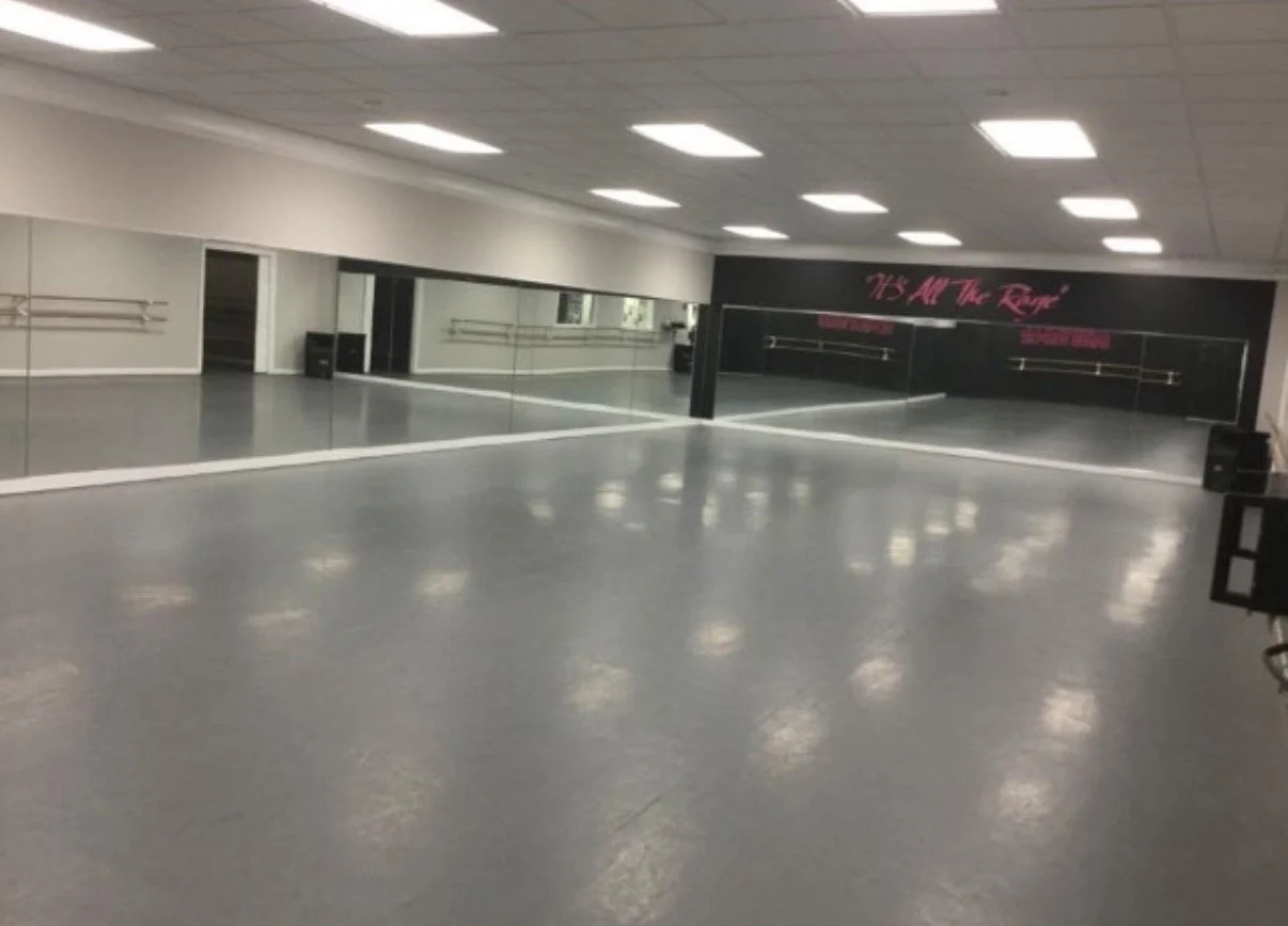 Empty dance studio with mirrors on the wall, ballet barres, and a sign that says 'It's All The Rage'