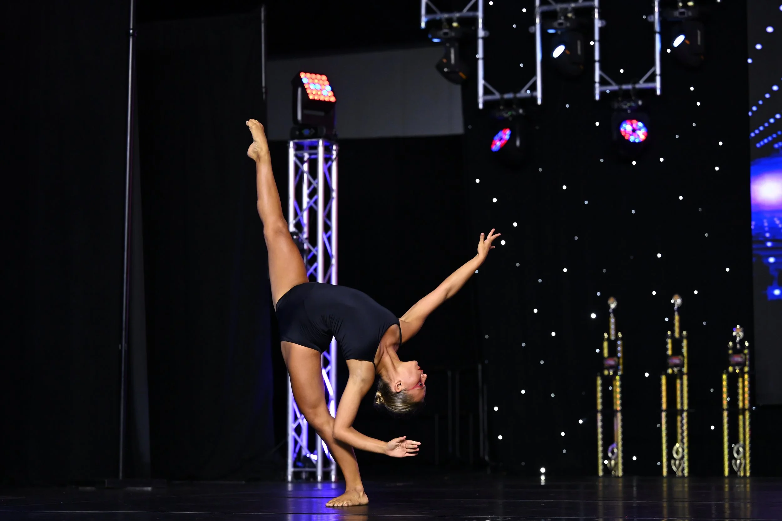 A female acrobat performing a handstand on stage, with stage lighting and equipment in the background.