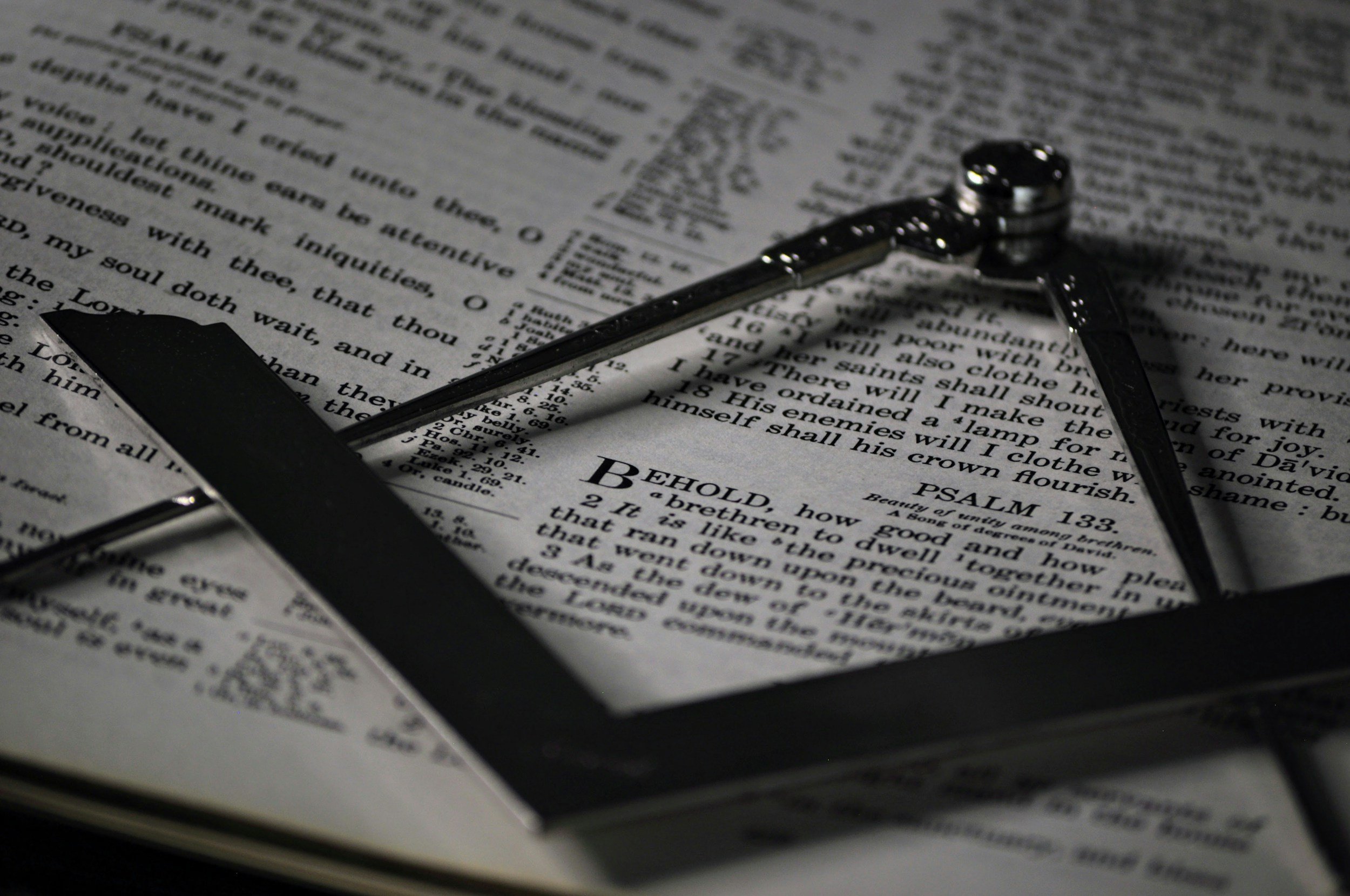 Close-up of a black and silver compass resting on an open Bible with text visible, including a verse from Psalms.