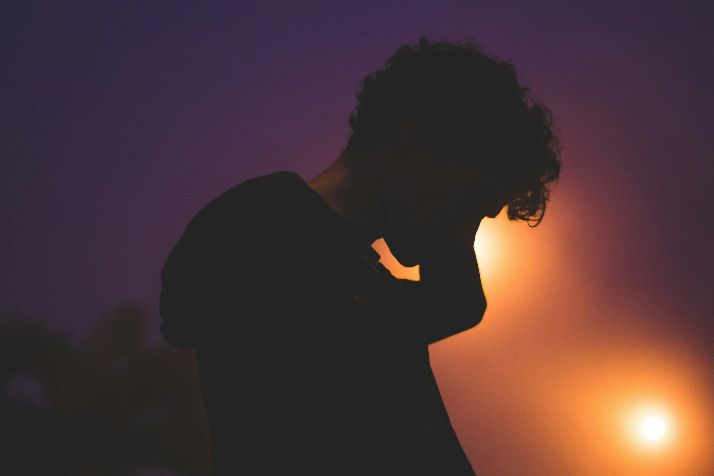 Silhouette of a person with curly hair against a sunset or sunrise sky.