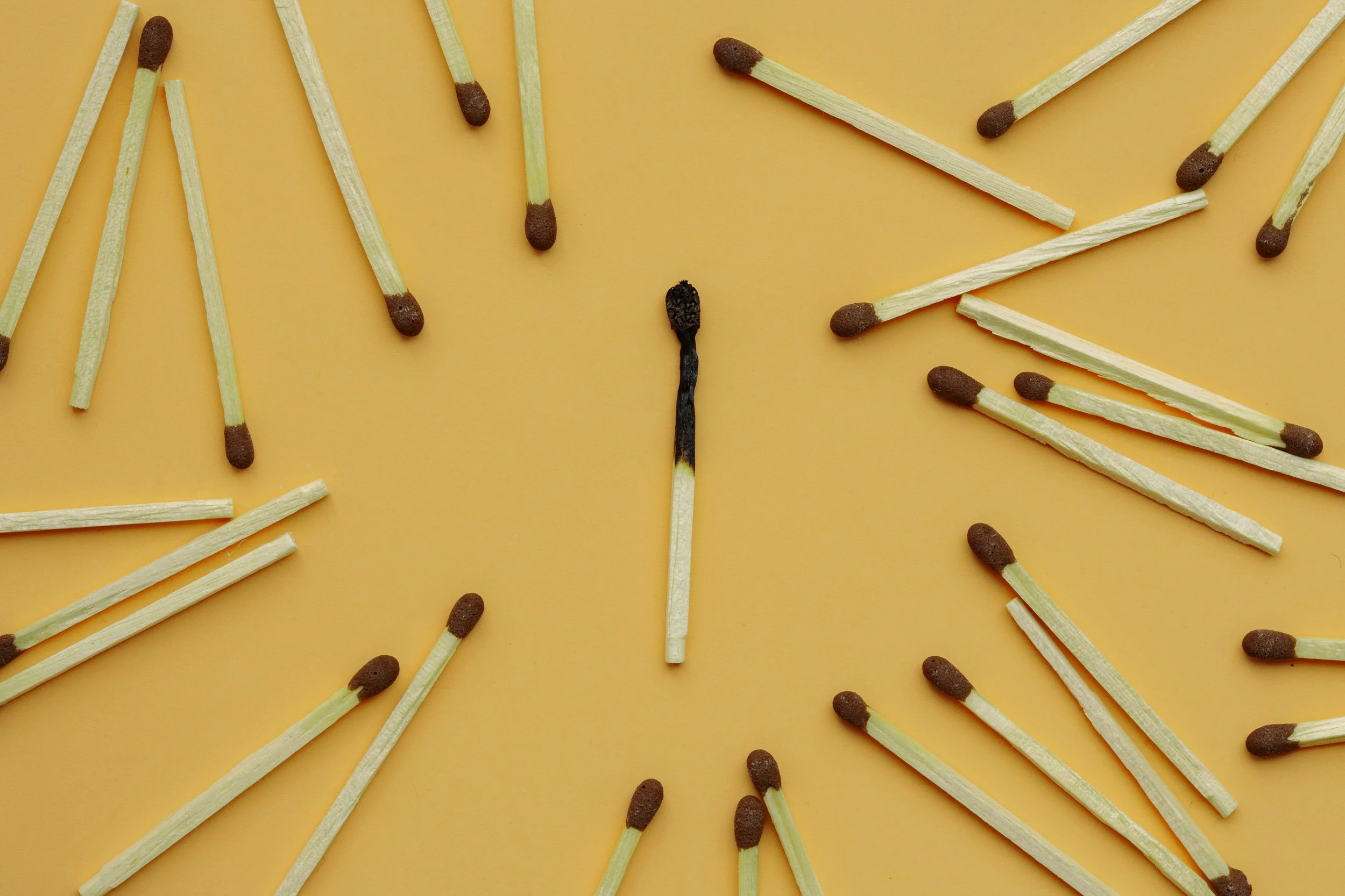 Multiple wooden matches scattered on a yellow surface, with some matches burned and blackened.