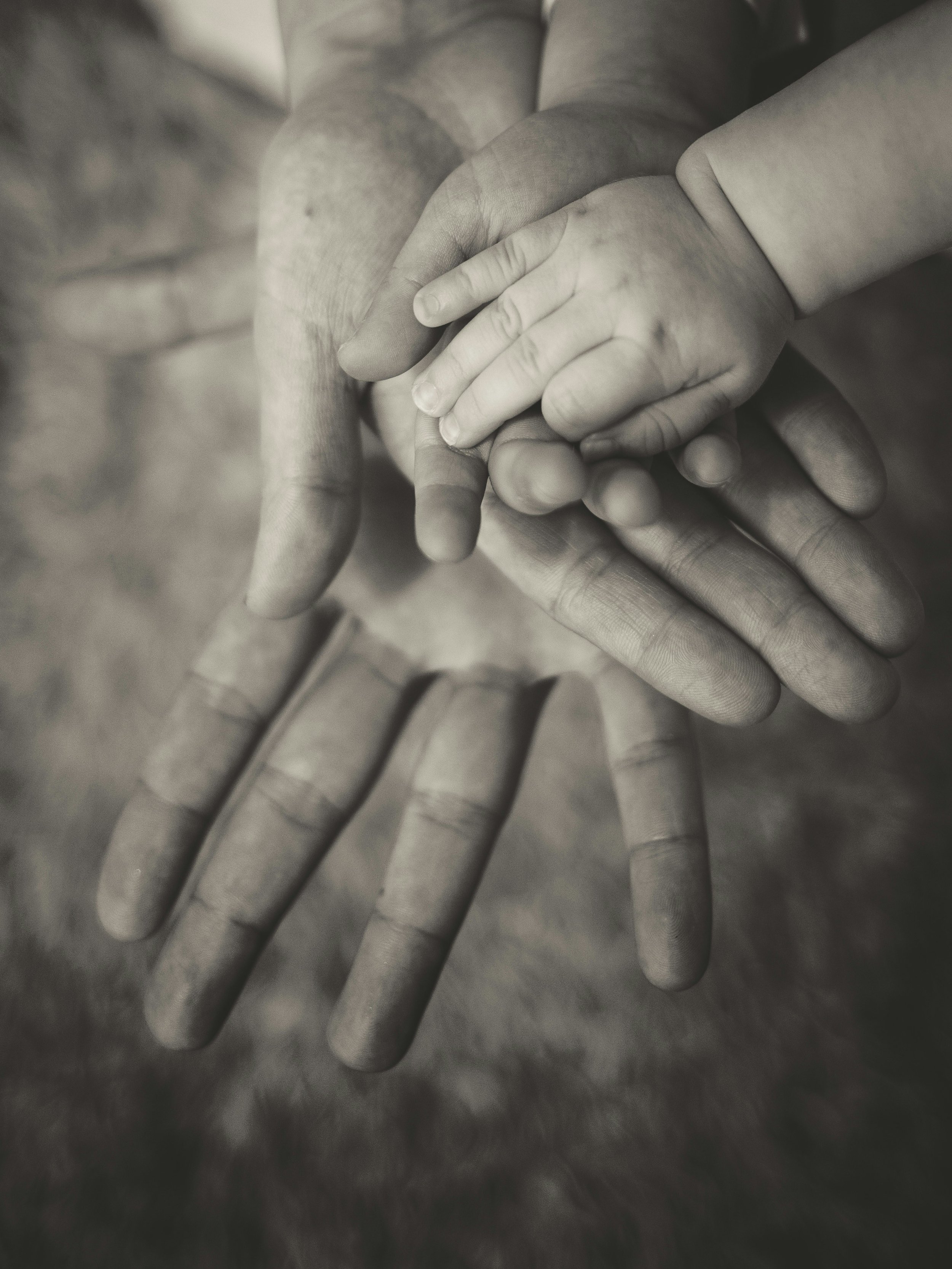 Close-up of a child's hand holding an adult's finger, with both standing on a reflective surface.