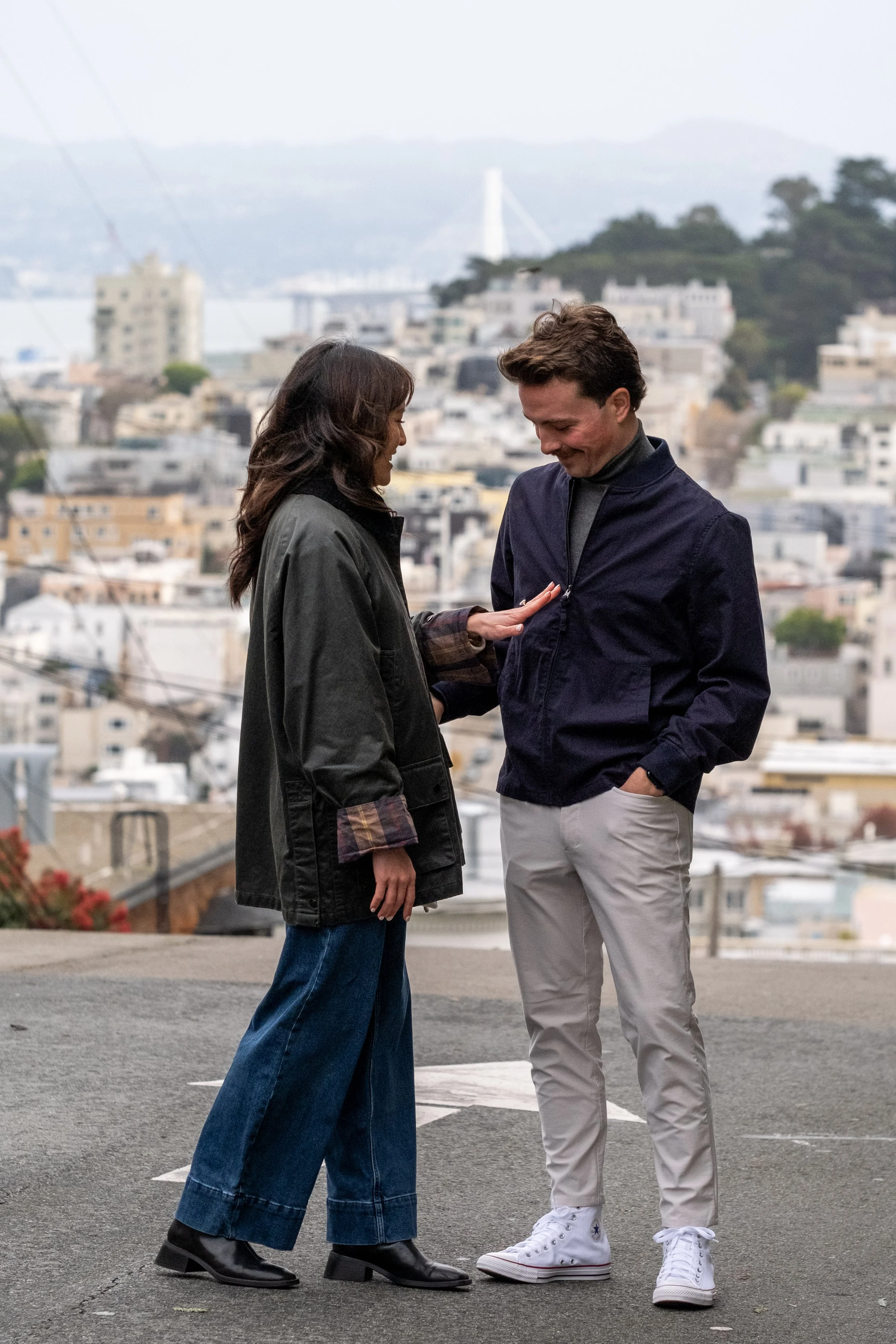 A couple admiring the ring after the man proposes to the woman, during a surprise proposal photoshoot with San Francisco views behind them.