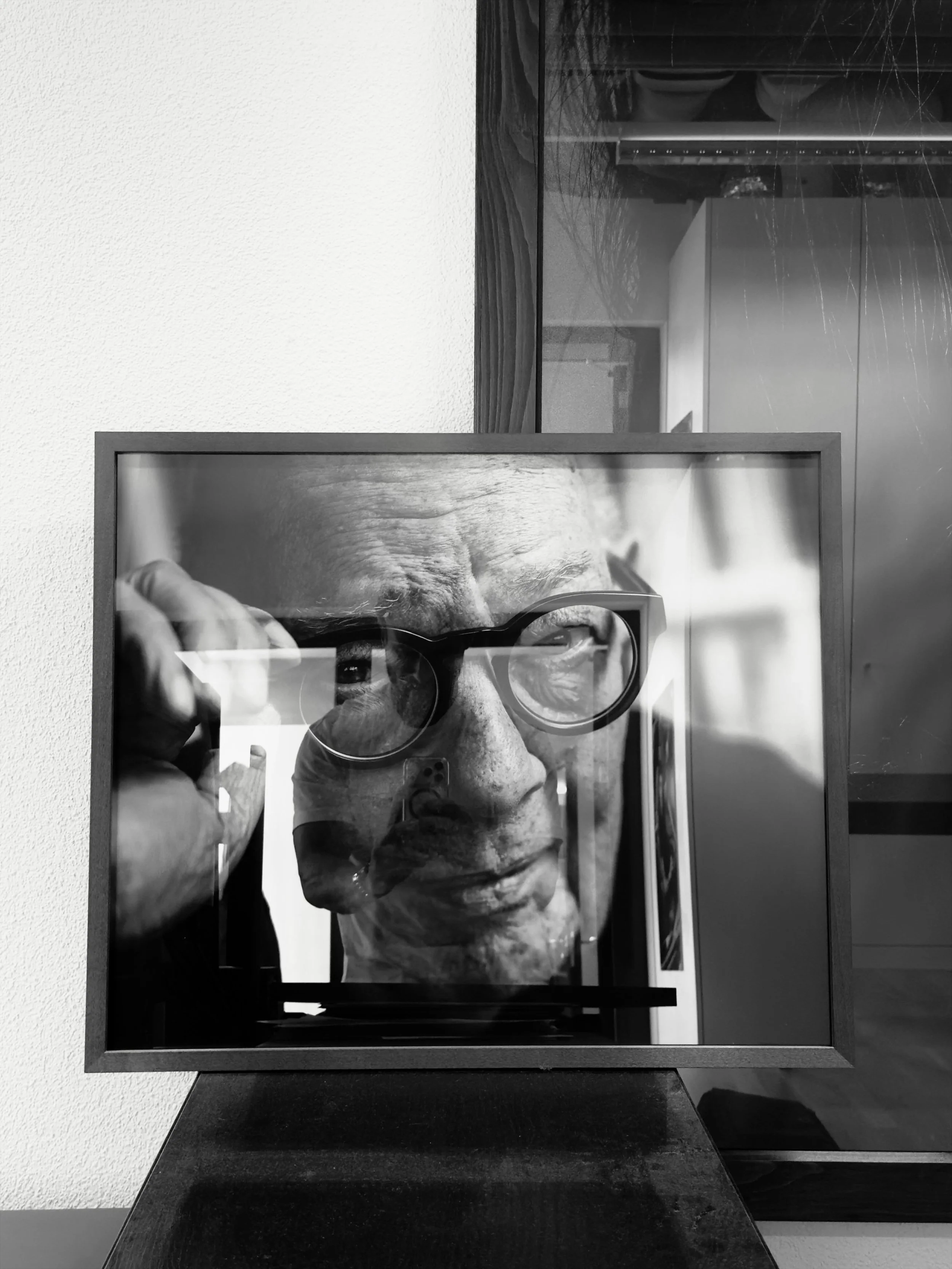 Schwarz-Weiß-Fotografie eines Mannes, der eine Brille trägt und ein Selfie im Spiegel macht.