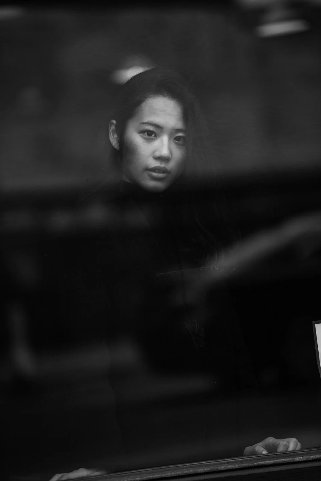 Schwarze und weiße Fotografie eines jungen asiatischen Mädchens, das durch eine Glasscheibe schaut.