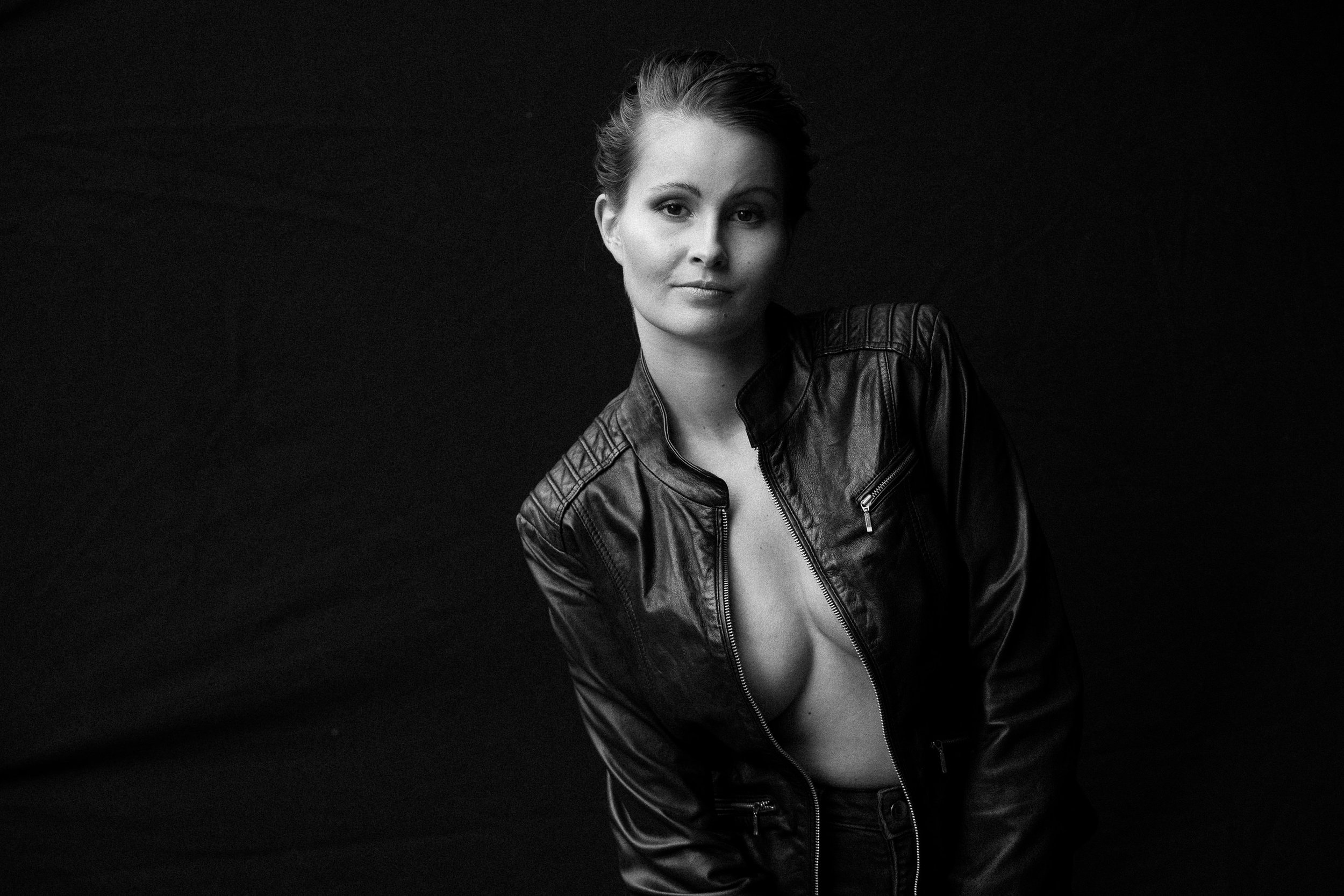 Schwarz-weiß Portrait einer Frau mit Kurzhaarfrisur in Lederjacke vor dunklem Hintergrund.