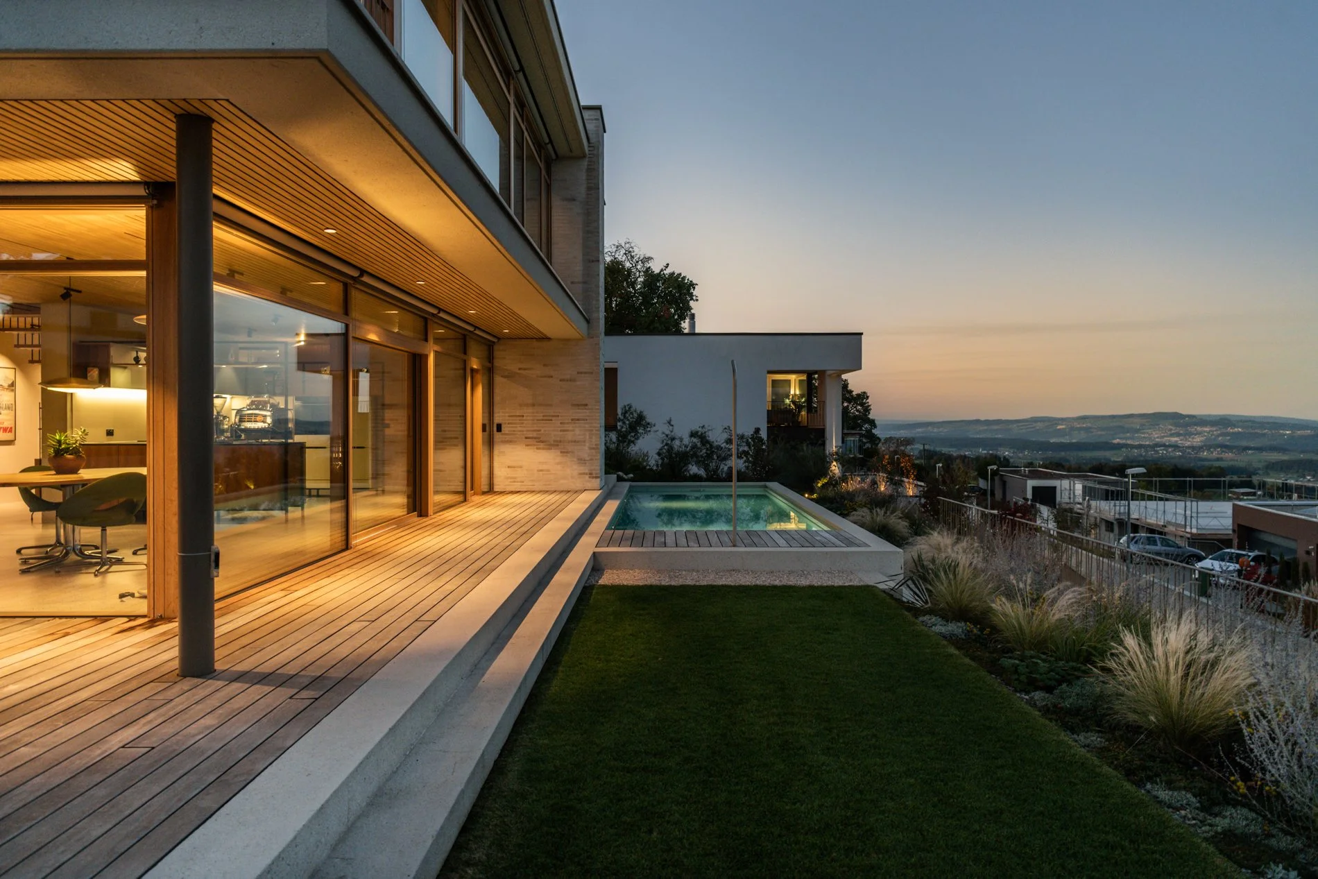 Moderne Villa mit Holzterrasse, einem kleinen Pool, großen Glasfenstern und einem weiten Blick bei Sonnenuntergang.