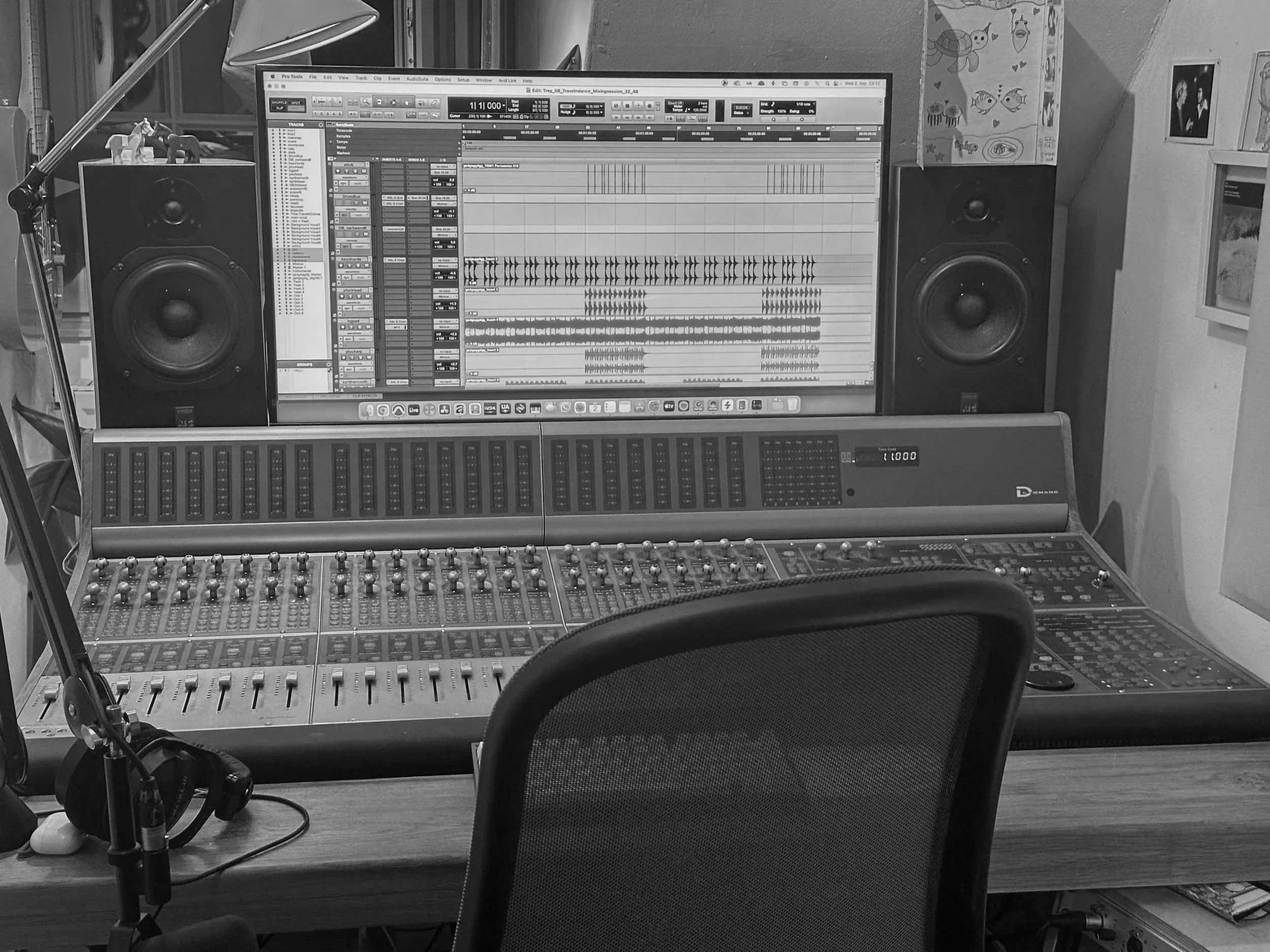 A computer monitor displaying digital audio workstation software with multiple tracks and waveforms, surrounded by studio equipment including a mixing console, speakers, a microphone, and a guitar on a stand, in a music production studio.