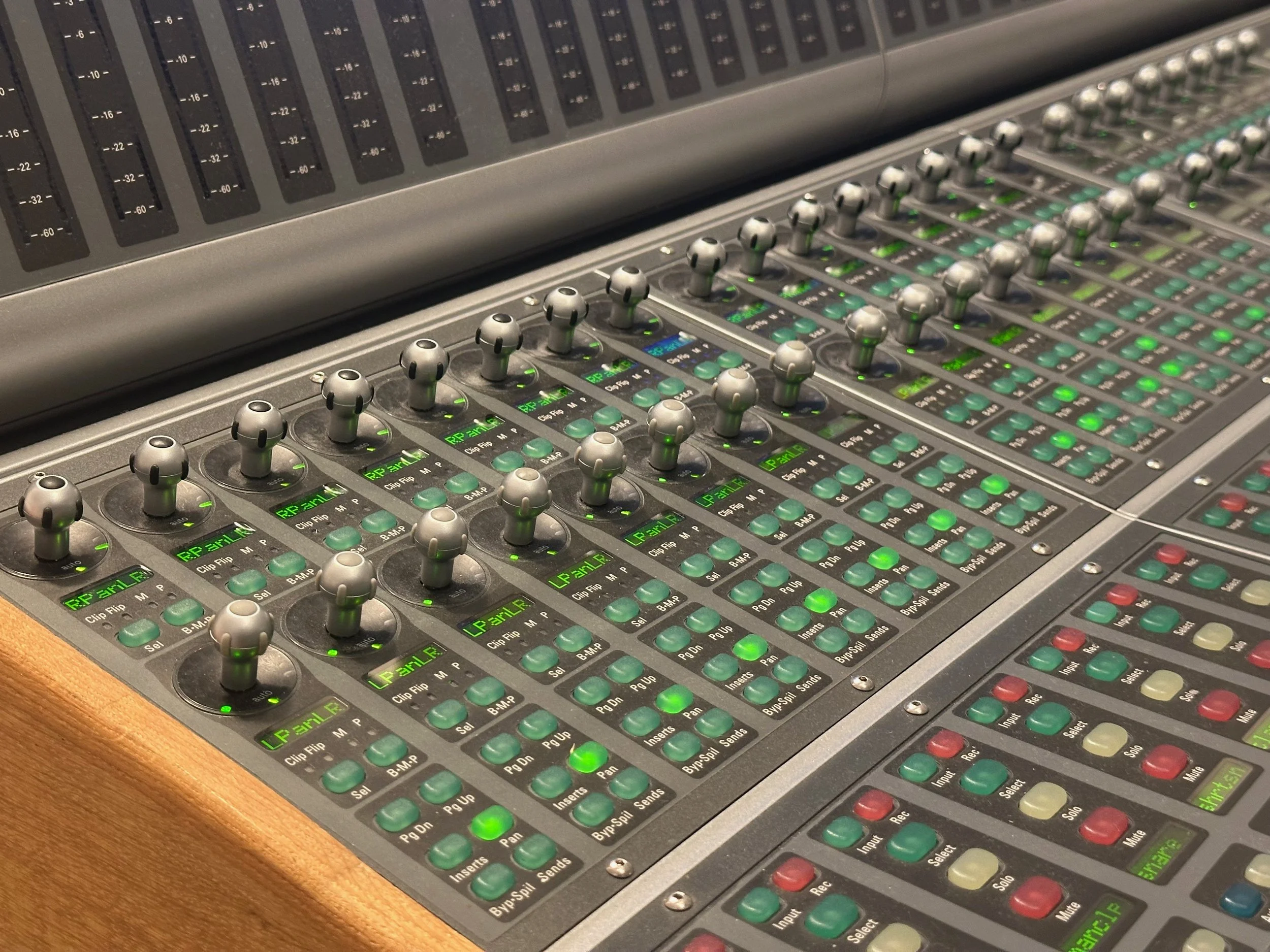 An audio mixing console with multiple sliders, knobs, and green LED indicators.