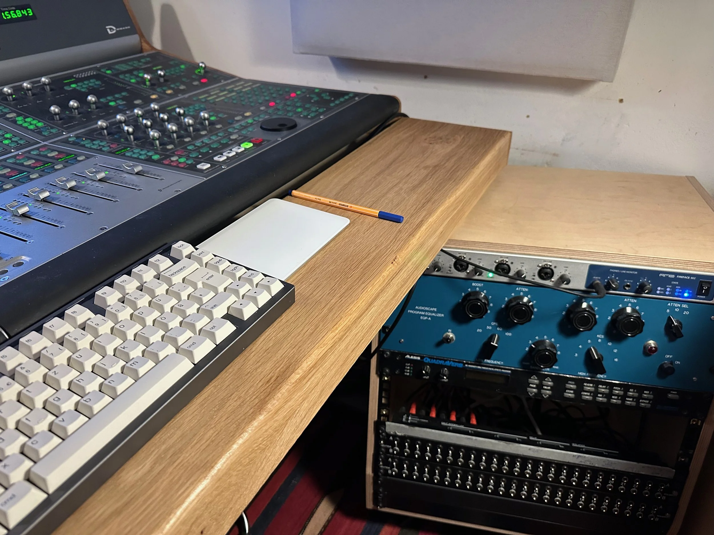 Music production workspace with a keyboard, audio mixing console, and audio equipment on wooden shelves.