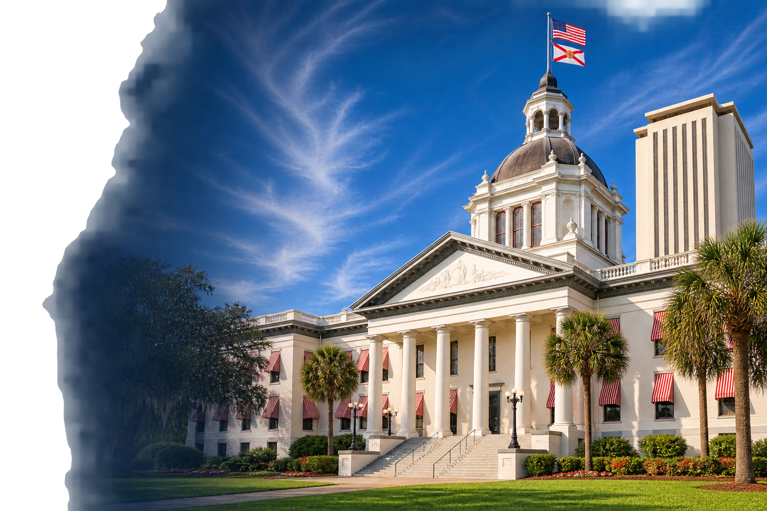 A white historic building with a dome, columns, and flags, surrounded by palm trees and a well-maintained lawn, under a blue sky with wispy clouds.