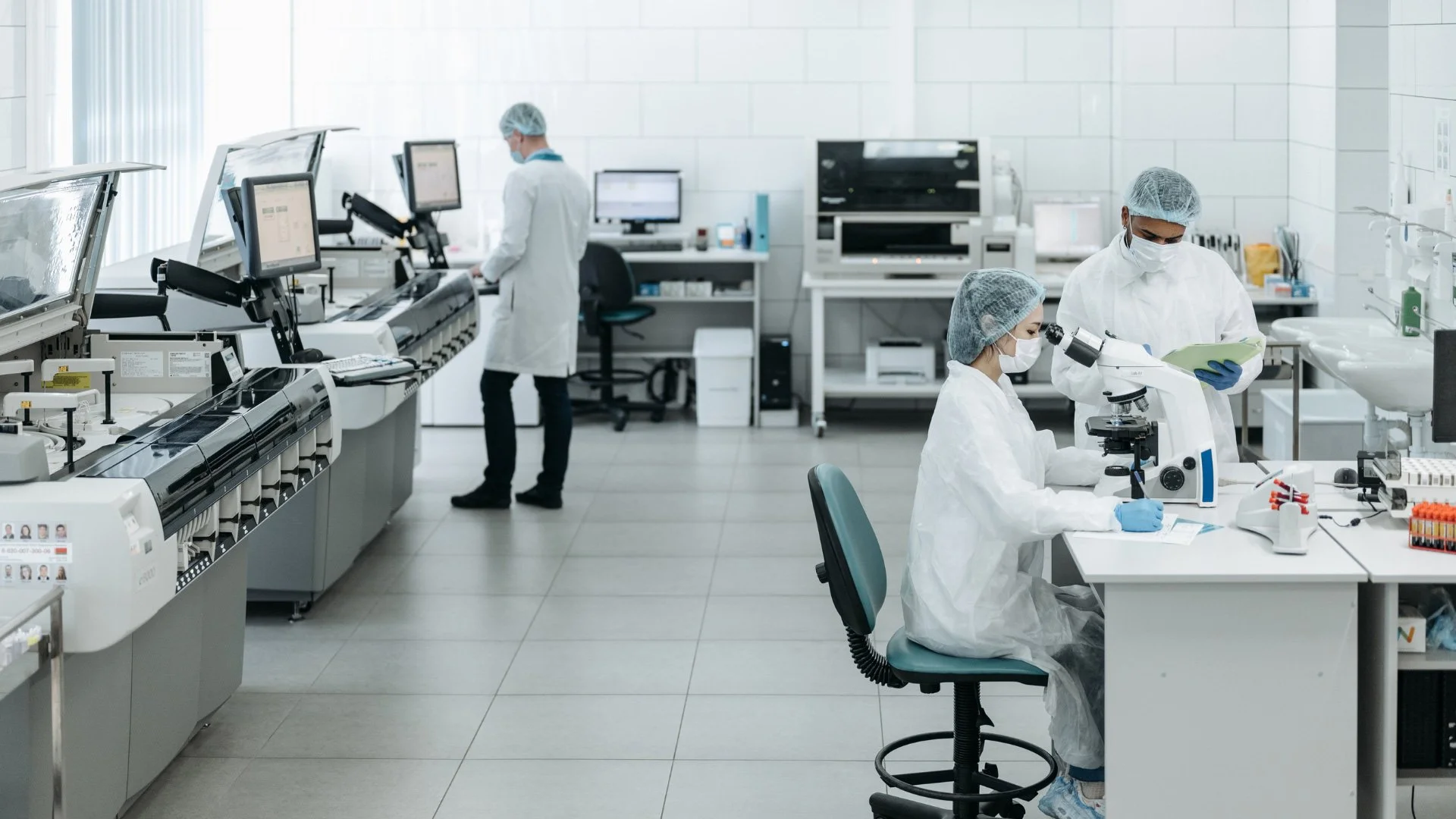 Scientists in protective gear working in a clean laboratory with scientific equipment and microscopes.