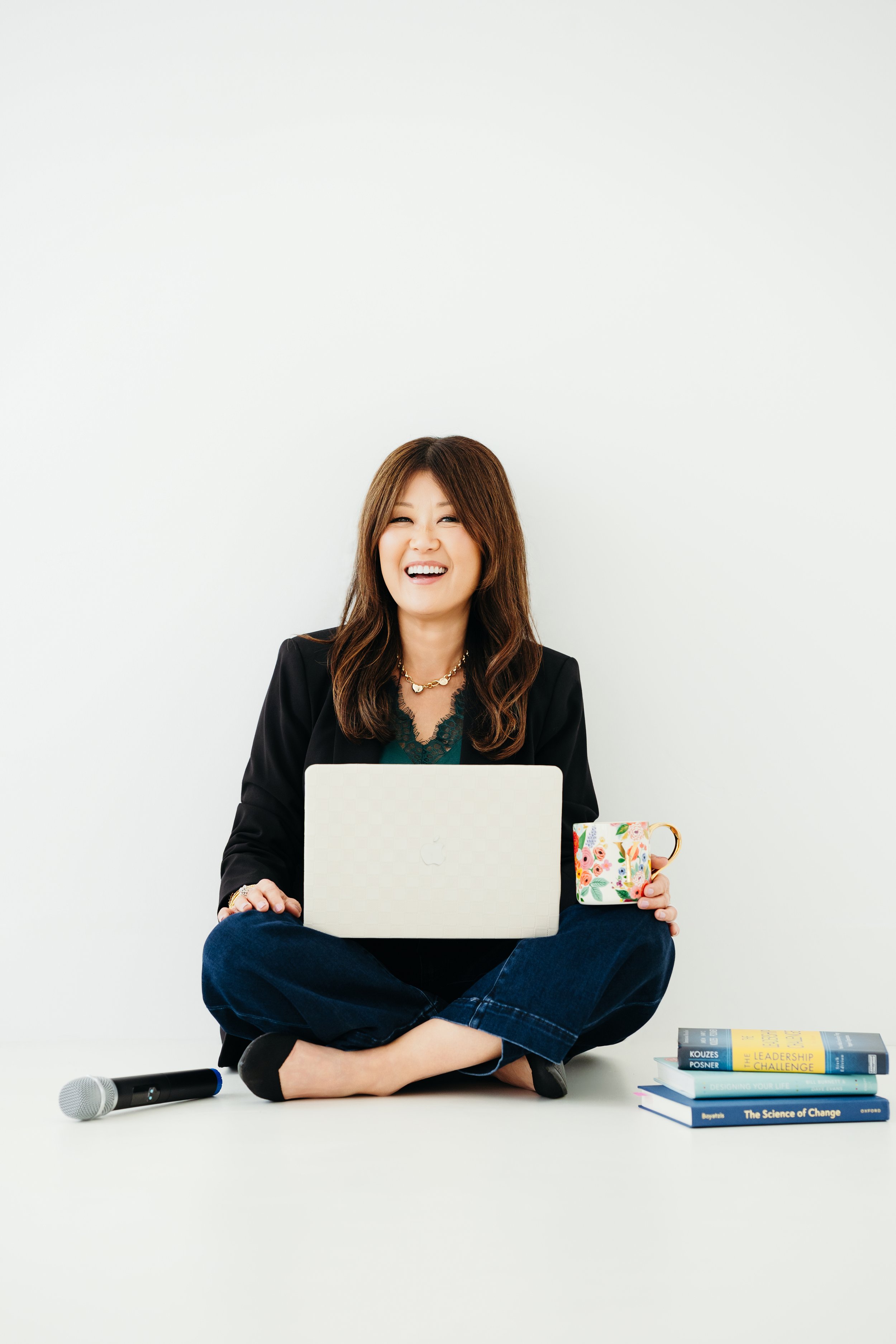 Yon Na, leadership coach and speaker, sitting on the floor with a laptop smiling