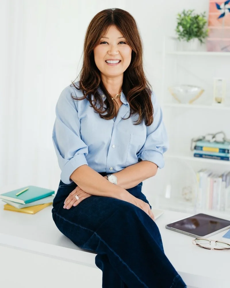 Dr. Yon Na, founder of Radiance Leadership, sitting on a white table in a home smiling