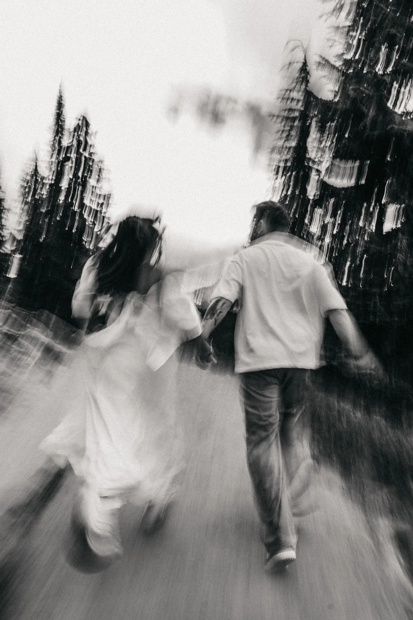 A black and white photo of three children holding hands and running outdoors, surrounded by tall trees.