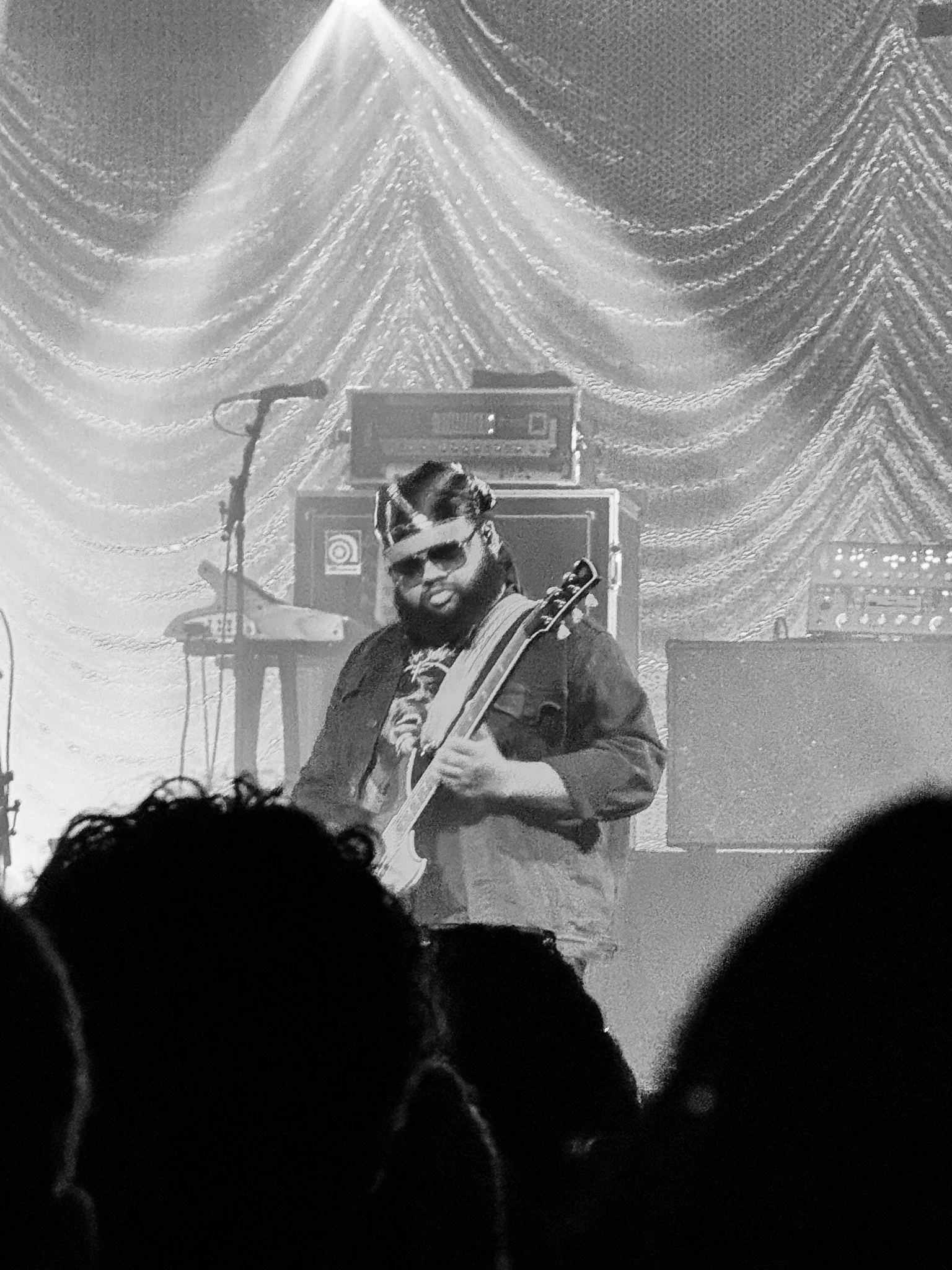 A musician playing a guitar on stage during a concert, with stage equipment and a decorative backdrop behind him.