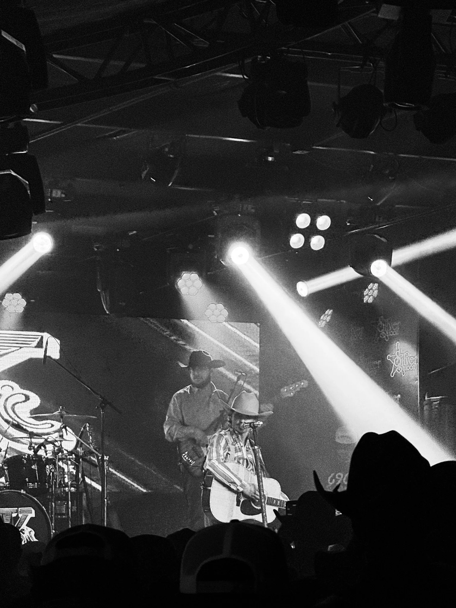 A musician wearing a cowboy hat and plaid shirt playing guitar on stage, with stage lights and equipment visible around him.
