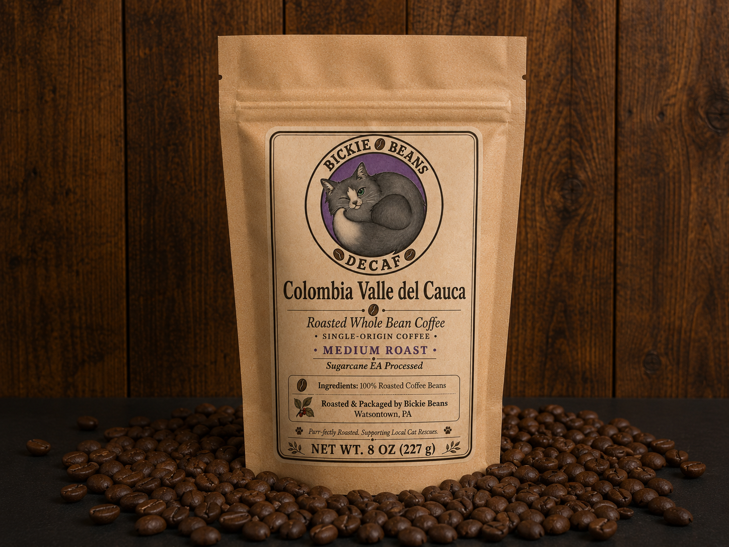 A package of Colombia Valle del Cauca roasted whole bean coffee with scattered coffee beans in front. The packaging features a drawing of a gray cat curled up, holding a coffee bean. The label provides details about the coffee's origin, roast level, and processing.