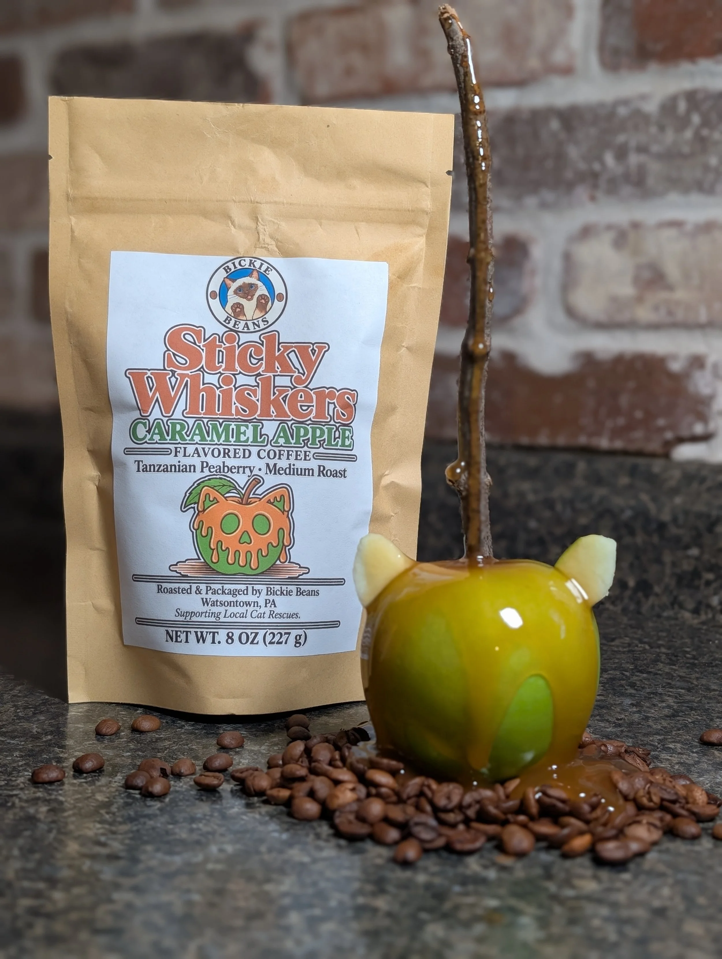 Bag of Bickie Beans Sticky Whiskers Caramel Apple coffee with a green cat-ear caramel apple and coffee beans on a granite counter