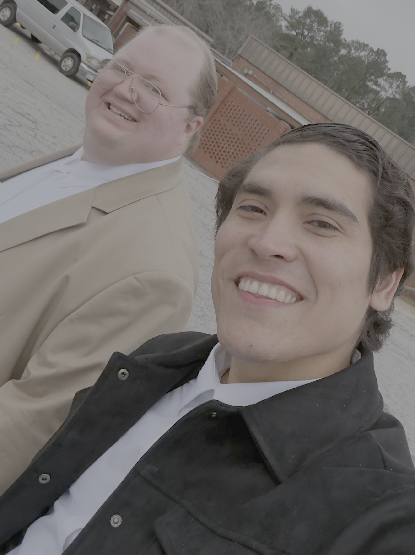 James Risner and his husband, David, taking a selfie outdoors on a cloudy day, smiling and looking at the camera.