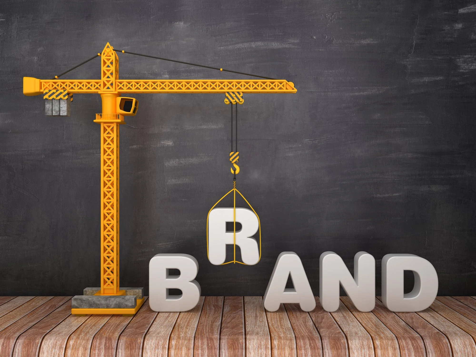 A yellow construction crane lifting a white letter R, with large white letters spelling 'B-AND' visible on the floor beneath it, set against a gray wall background and wooden floor.