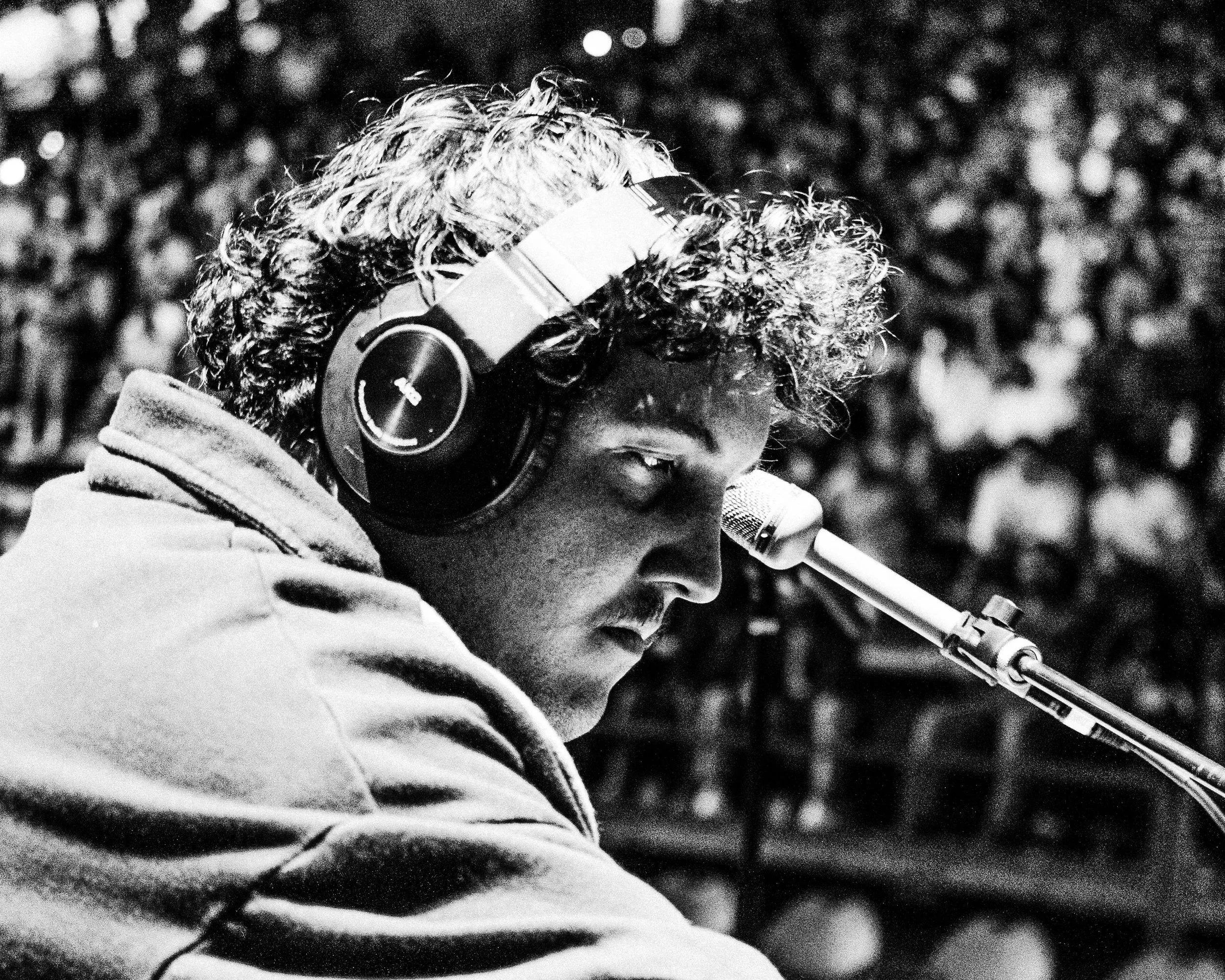 A black and white photo of a young person with curly hair wearing headphones and looking into a telescope.