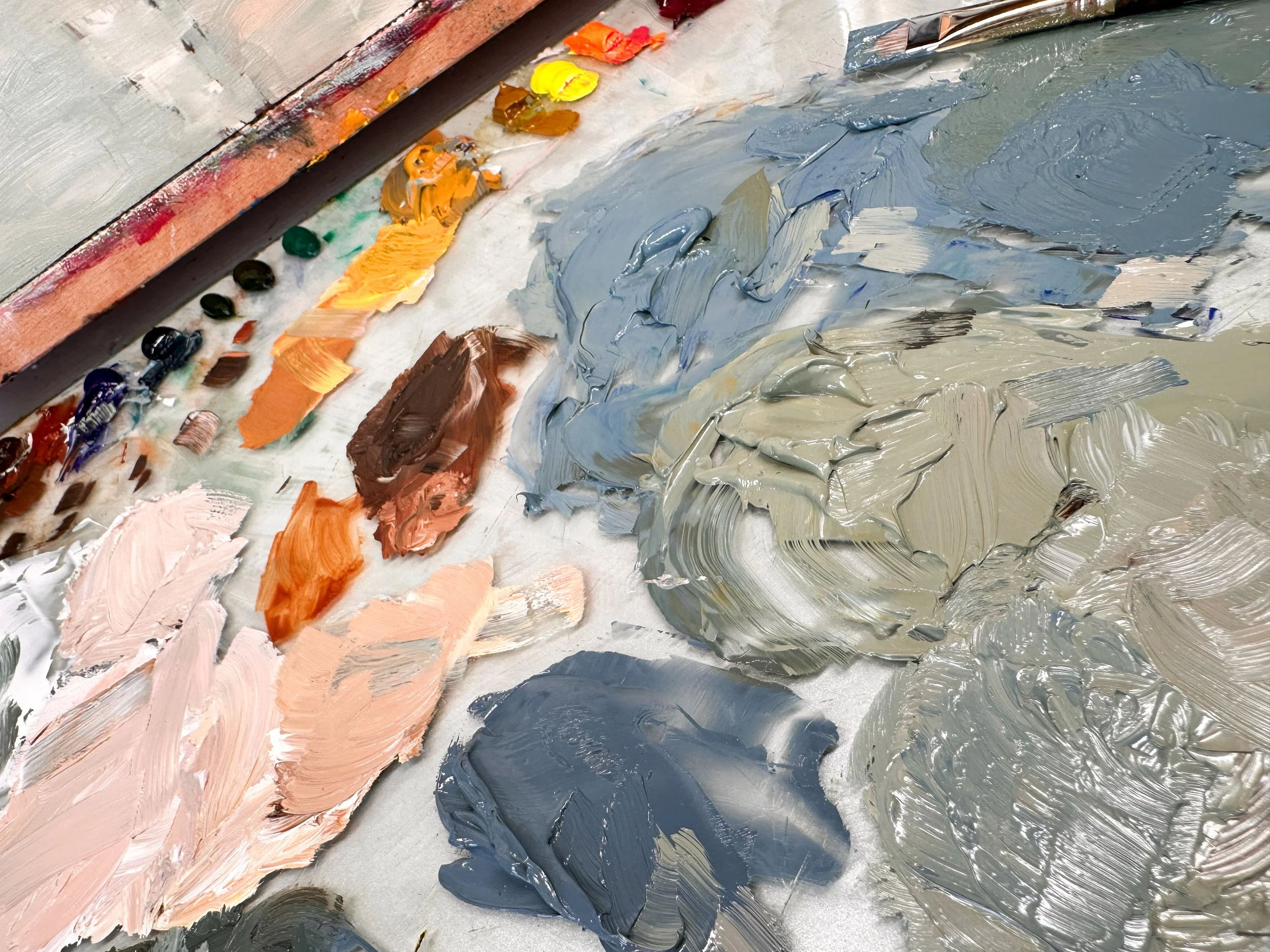 Artist’s palette with mixed oil paints in soft blues, warm neutrals, peach, and cream.