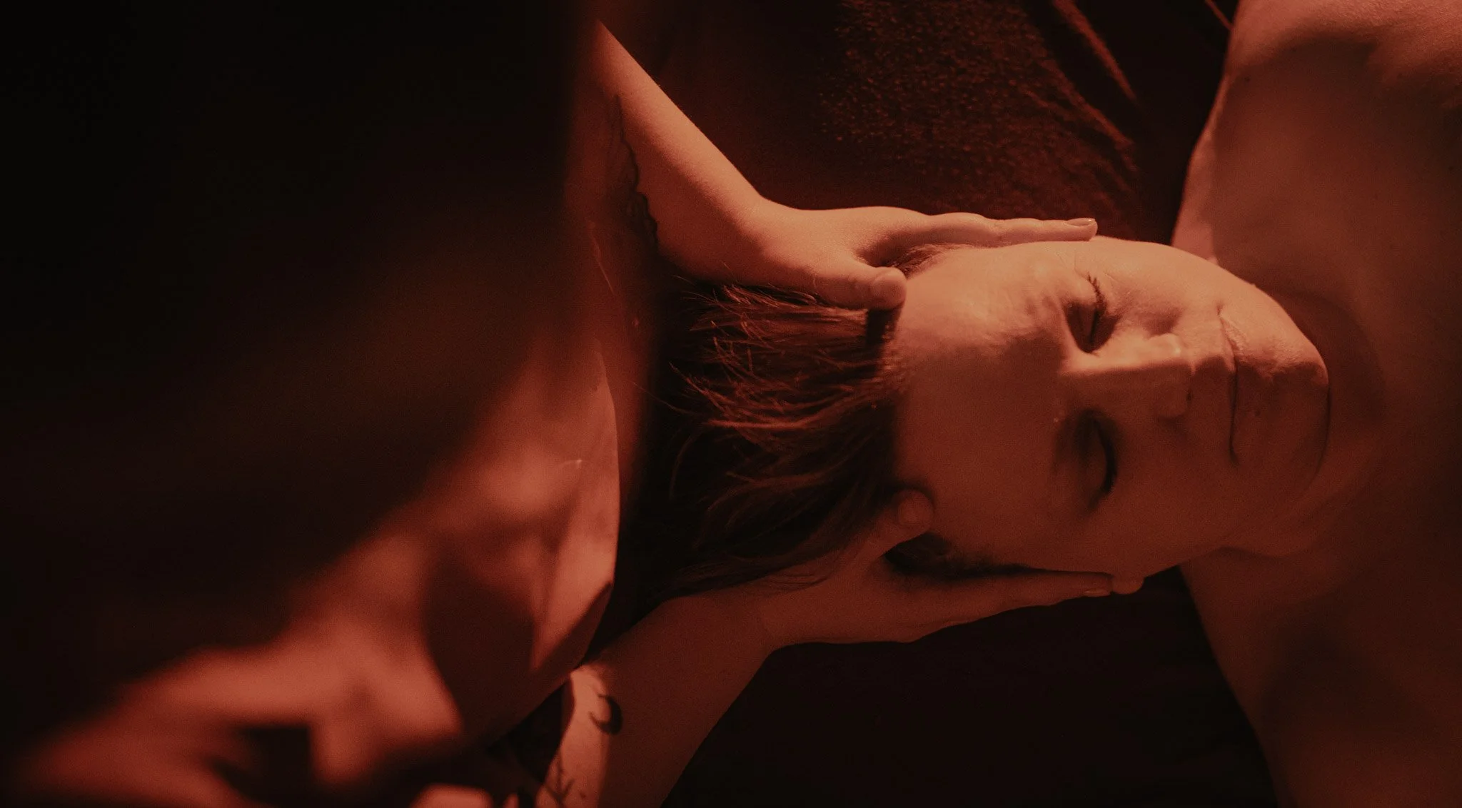 A woman with closed eyes lying down with dim, reddish lighting.