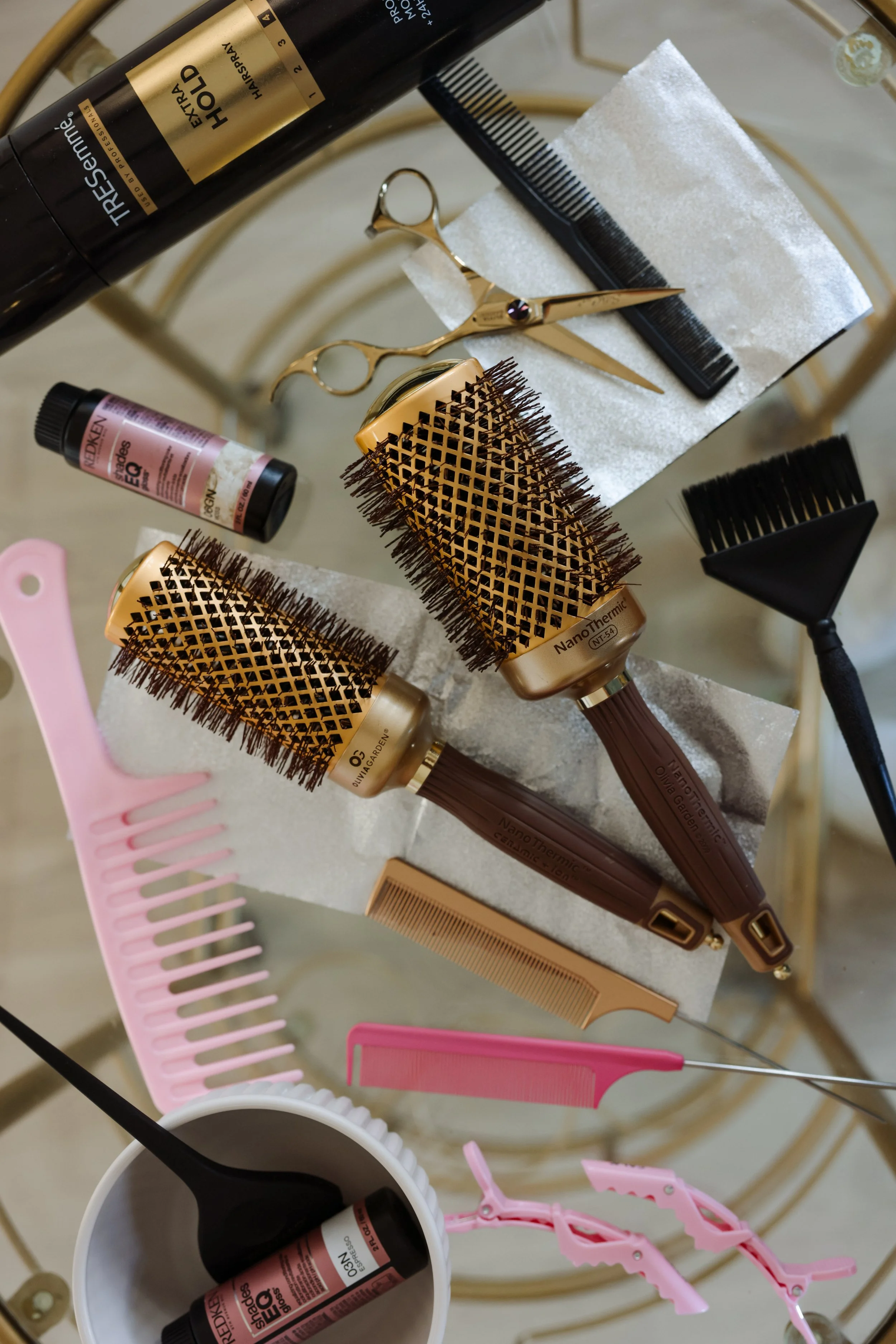 Hair styling tools including brushes, combs, scissors, clips, hair dye, and a spray bottle arranged on a surface.