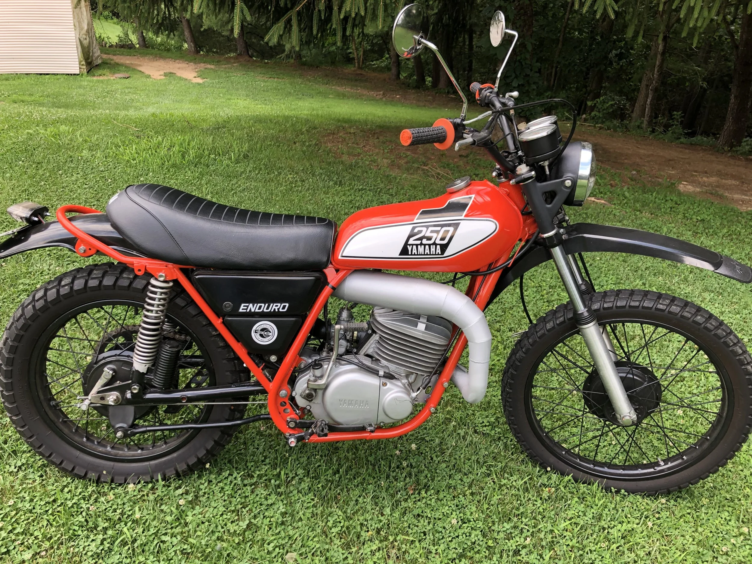 Red Yamaha 250 Enduro dirt bike parked on green grass with a wooded area in the background.