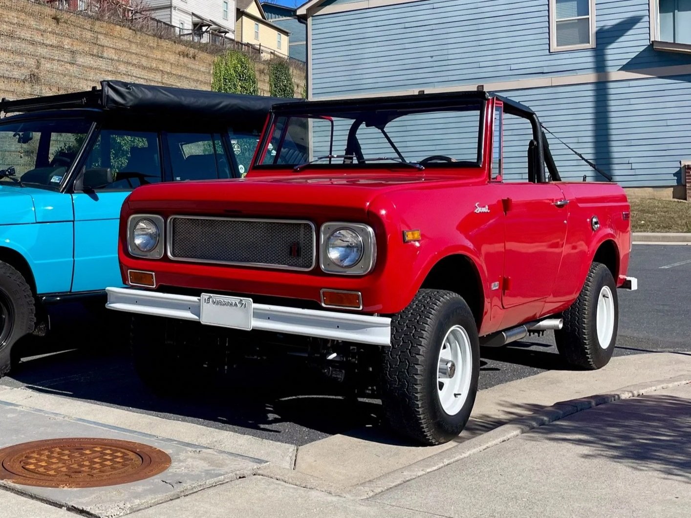 Red vintage utility truck parked next to a blue vehicle outdoors, with residential buildings in the background.