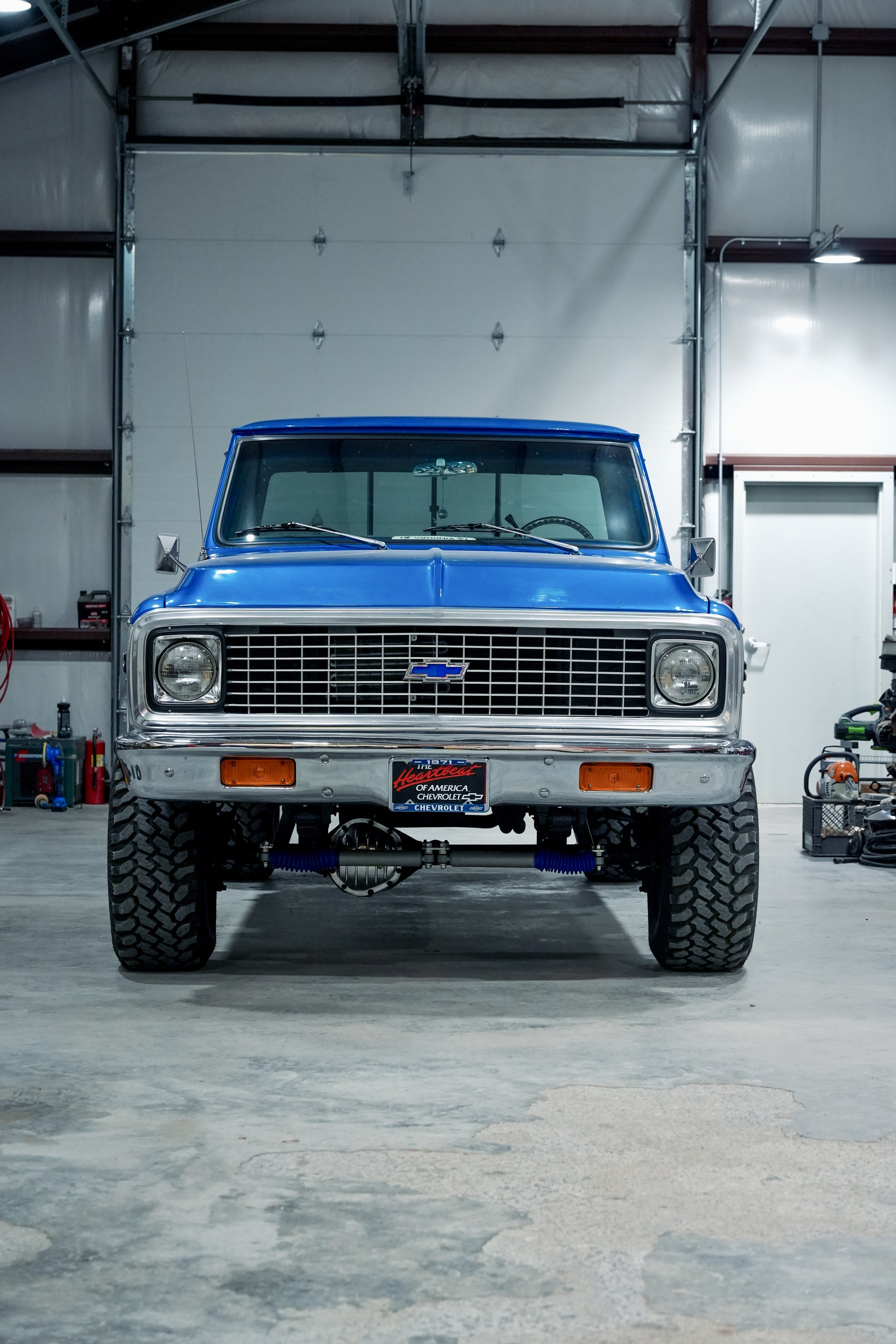 Front view of a vintage blue Chevrolet truck inside a workshop with tools and equipment on the shelves and floor.