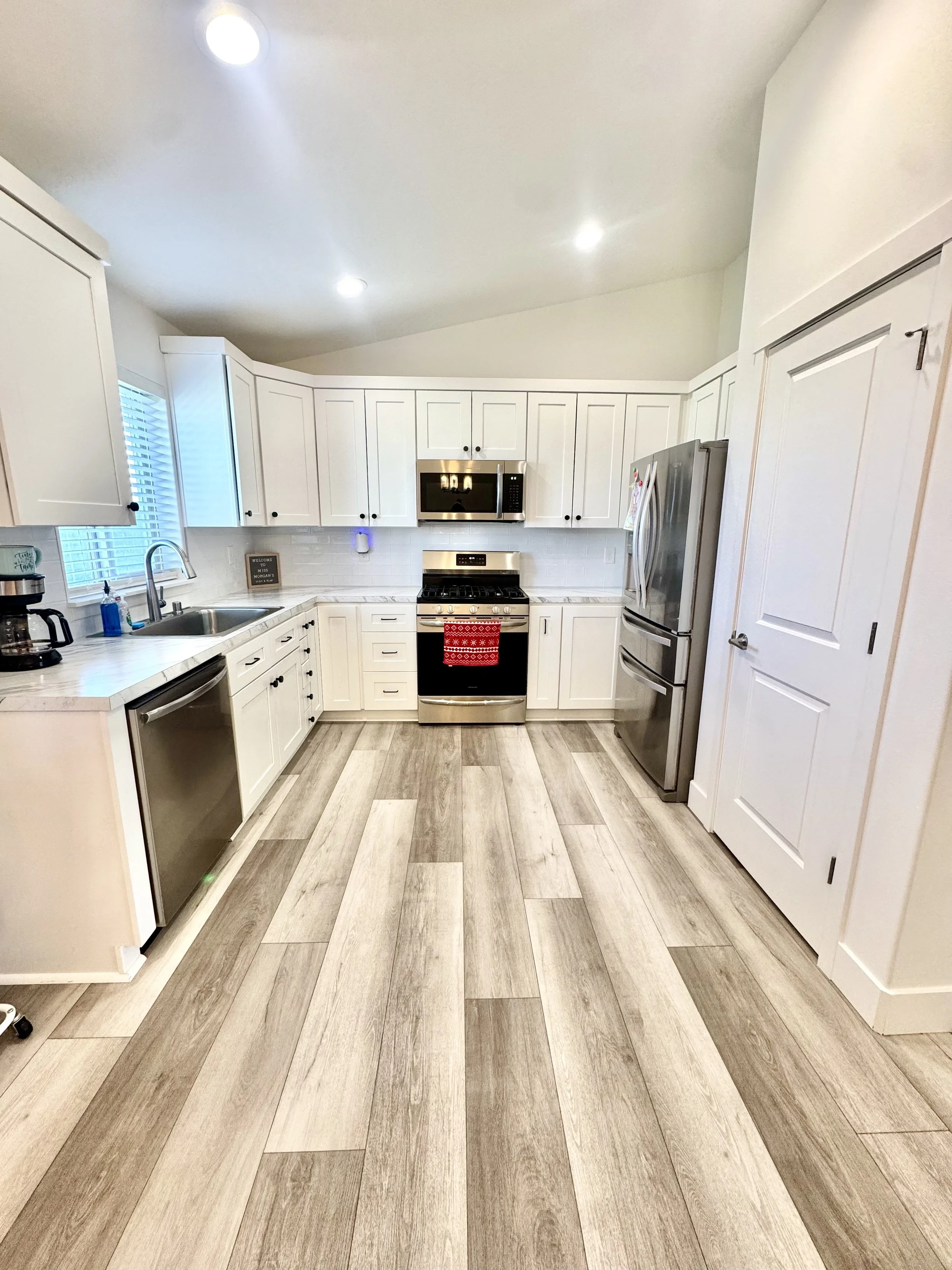 Kitchen with white cabinets, stainless steel appliances, gray wood-look tile flooring, and a window with blinds