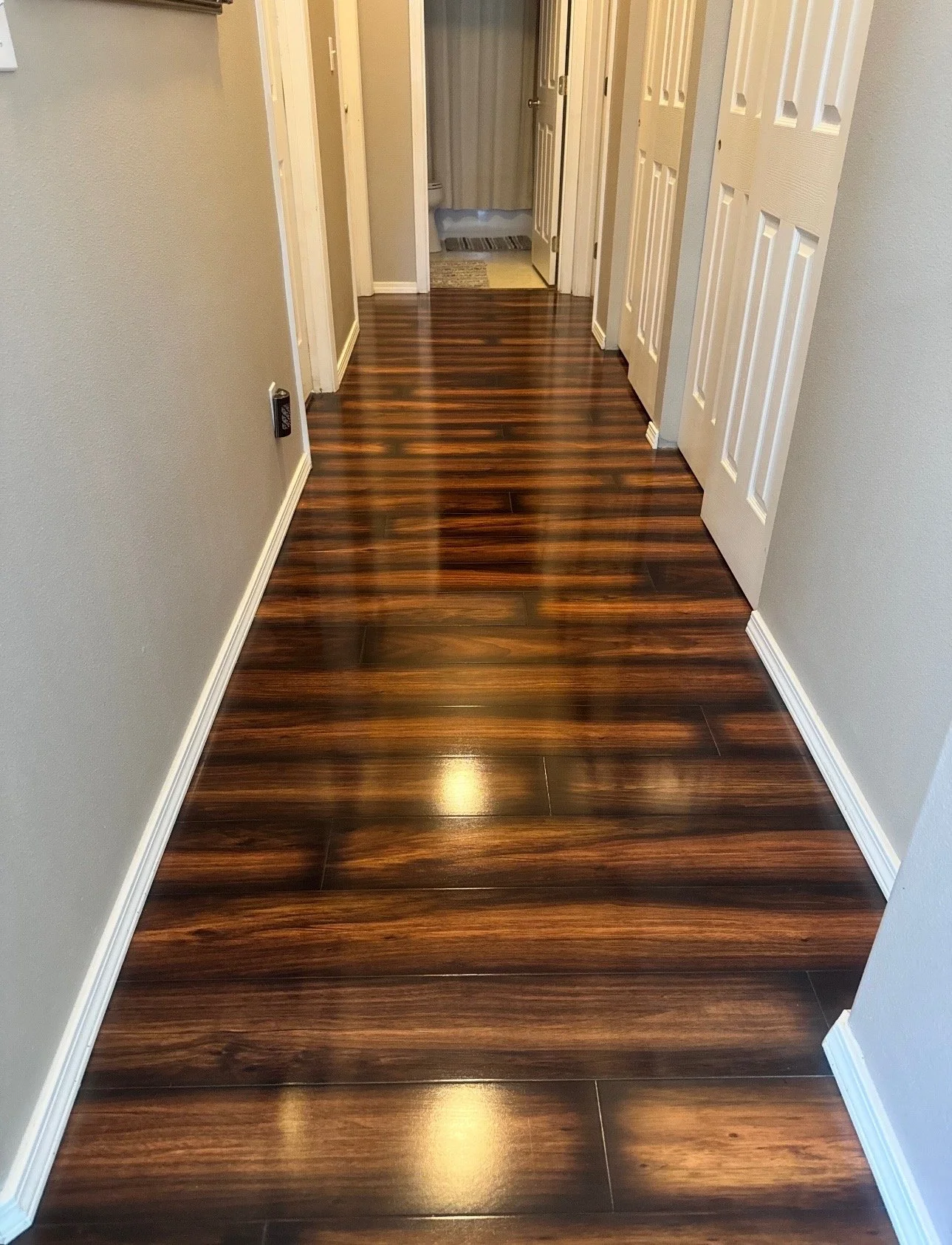 A hallway with polished dark wood flooring, light-colored walls, and white door frames.