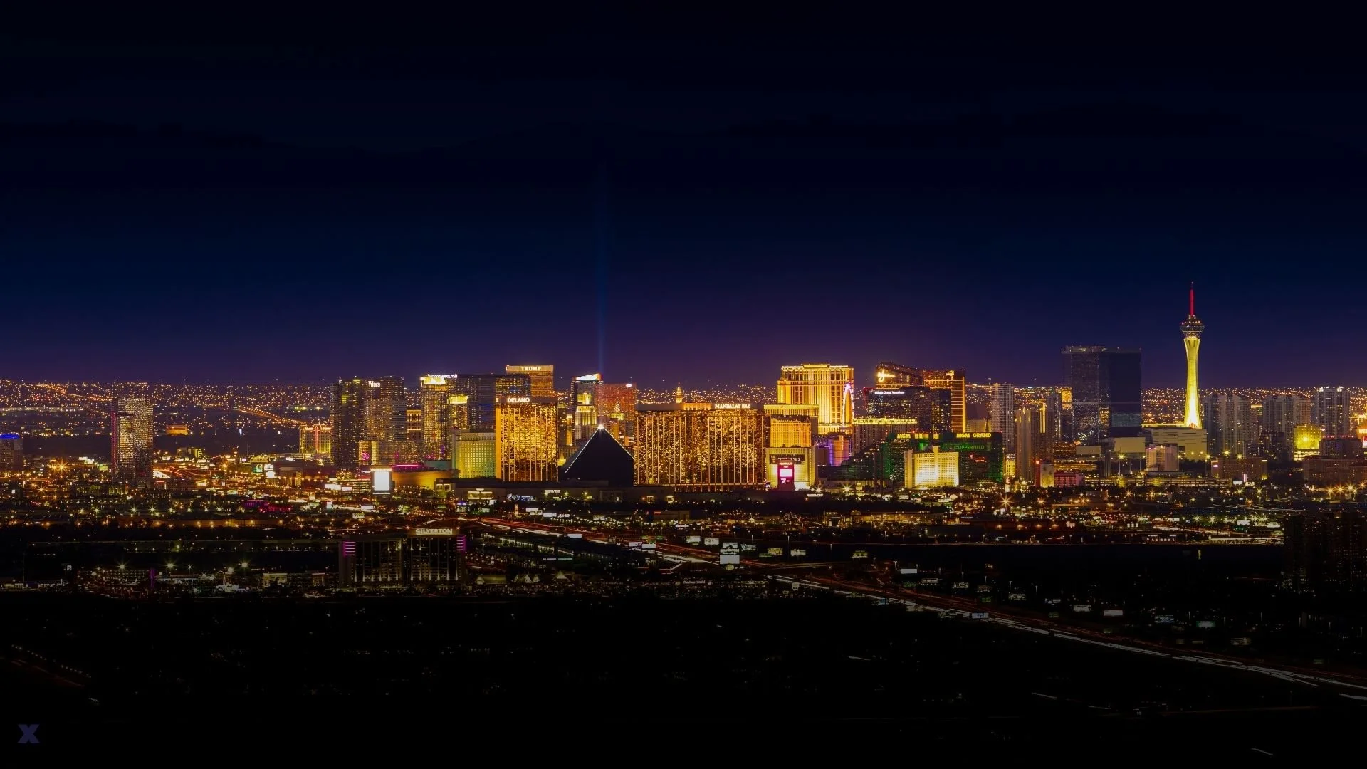 Nighttime view of the Las Vegas Strip with illuminated hotels and casinos, including the Luxor Pyramid and the Stratosphere Tower.